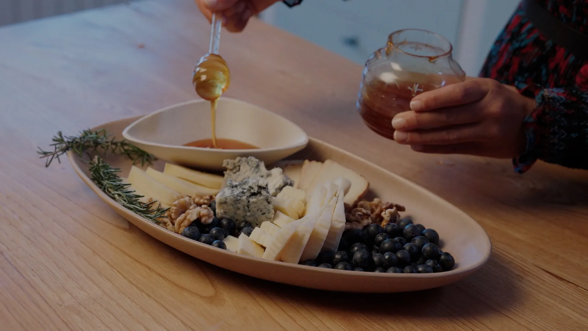 Miel cayendo sobre una tabla de quesos de Cantabria con arándanos, nueces y romero, servida en casa