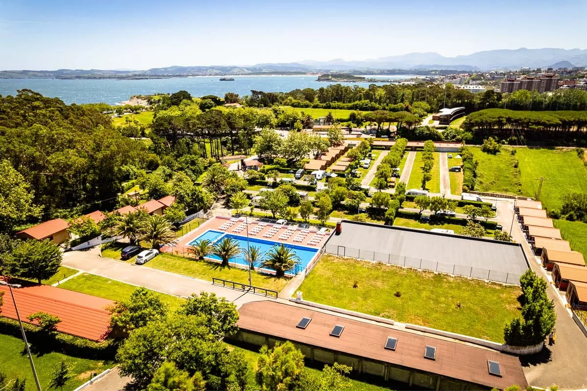 Vista aérea del Camping Cabo Mayor con la piscina y los bungalows, y la bahía de Santander al fondo