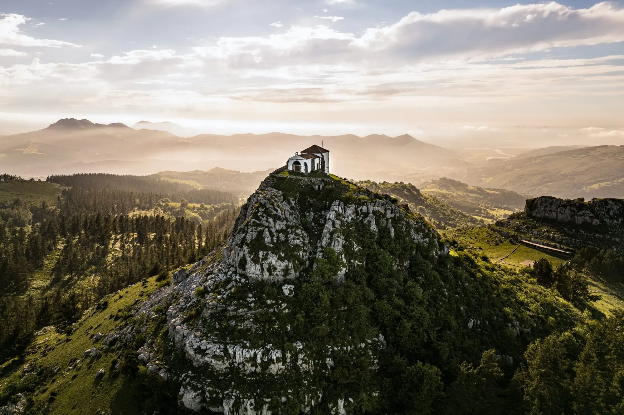 Ermita sobre un peñasco al atardecer, con los valles de la comarca Asón-Agüera-Trasmiera al fondo