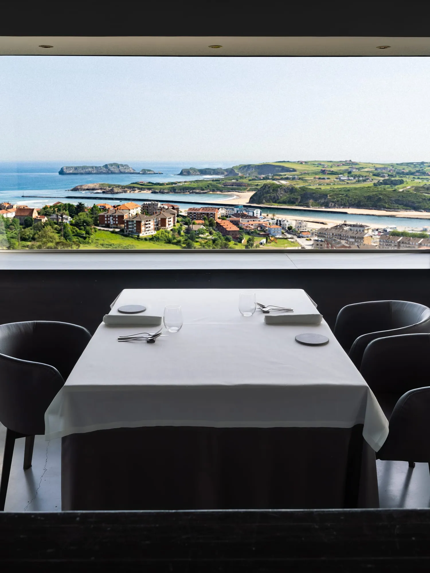Mesa vestida de blanco en el comedor de Emma, frente a un ventanal con vistas a la playa y la ría de Suances