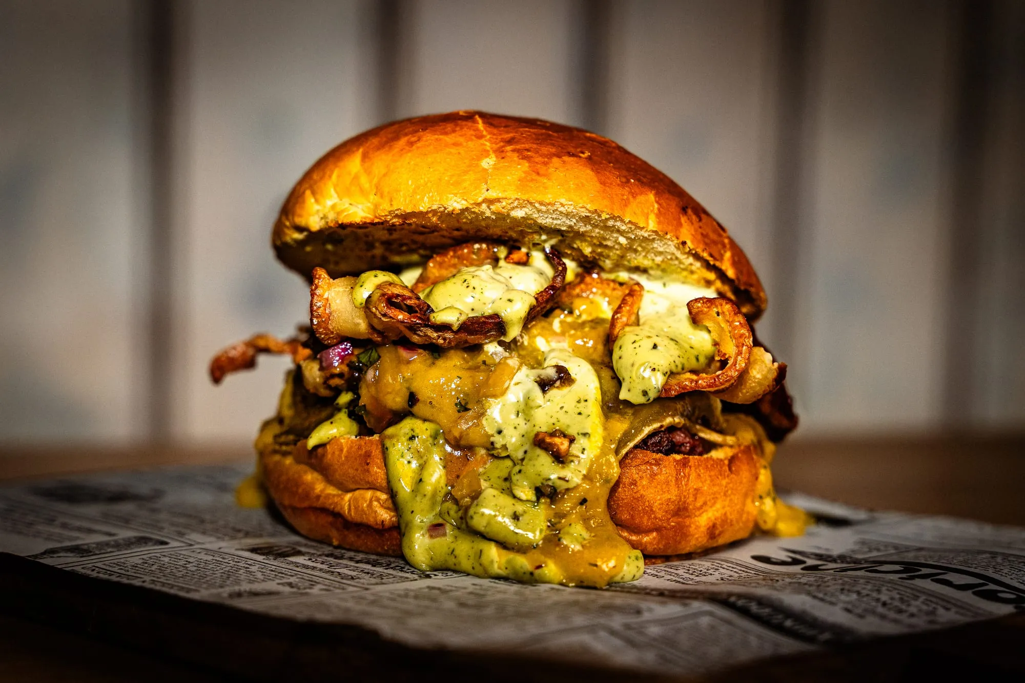 Hamburguesa con bacon y salsa de queso desbordando sobre una tabla de madera, con fondo negro