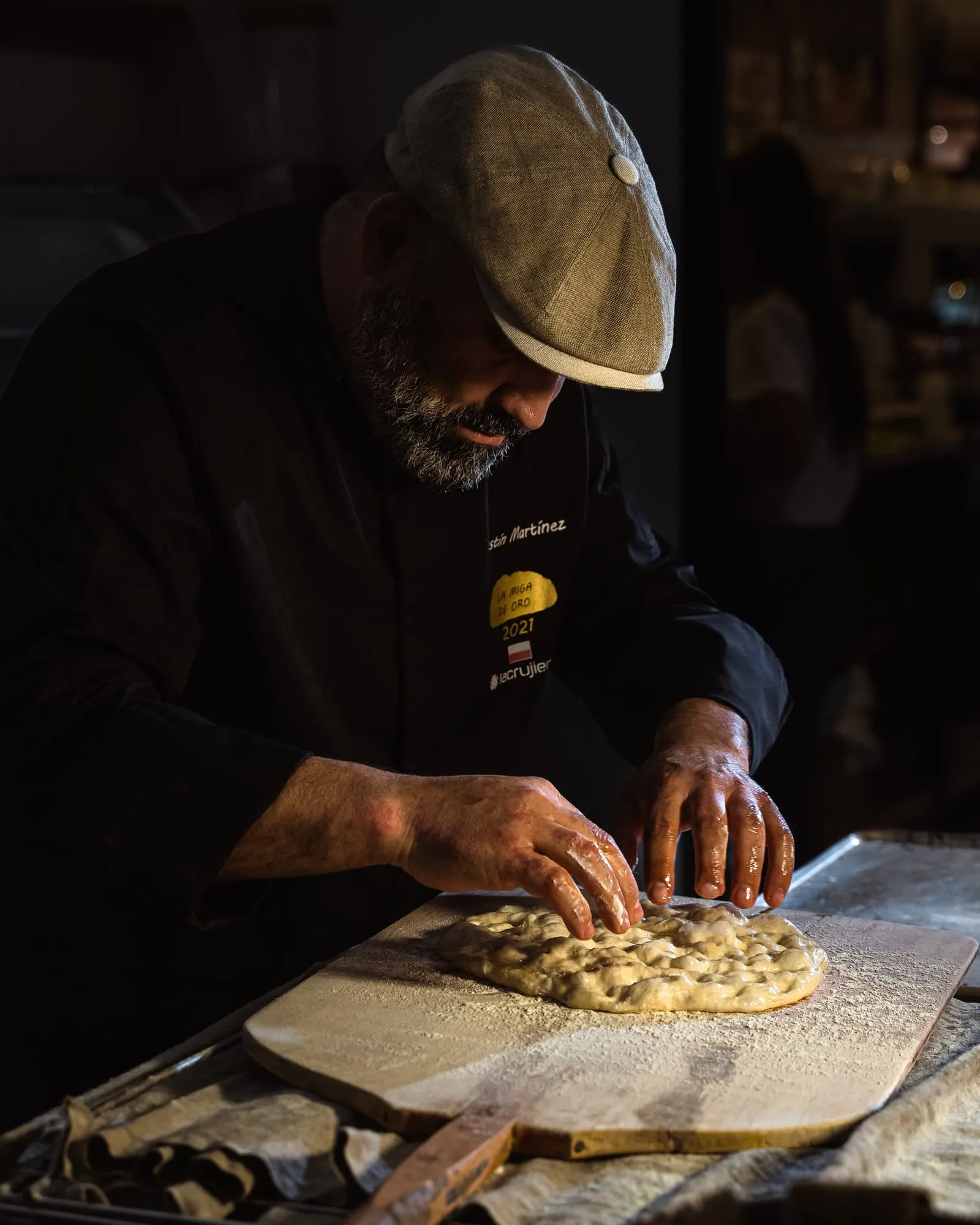 El panadero, con gorra y chaquetilla negra, marca con los dedos una masa sobre la pala de madera enharinada