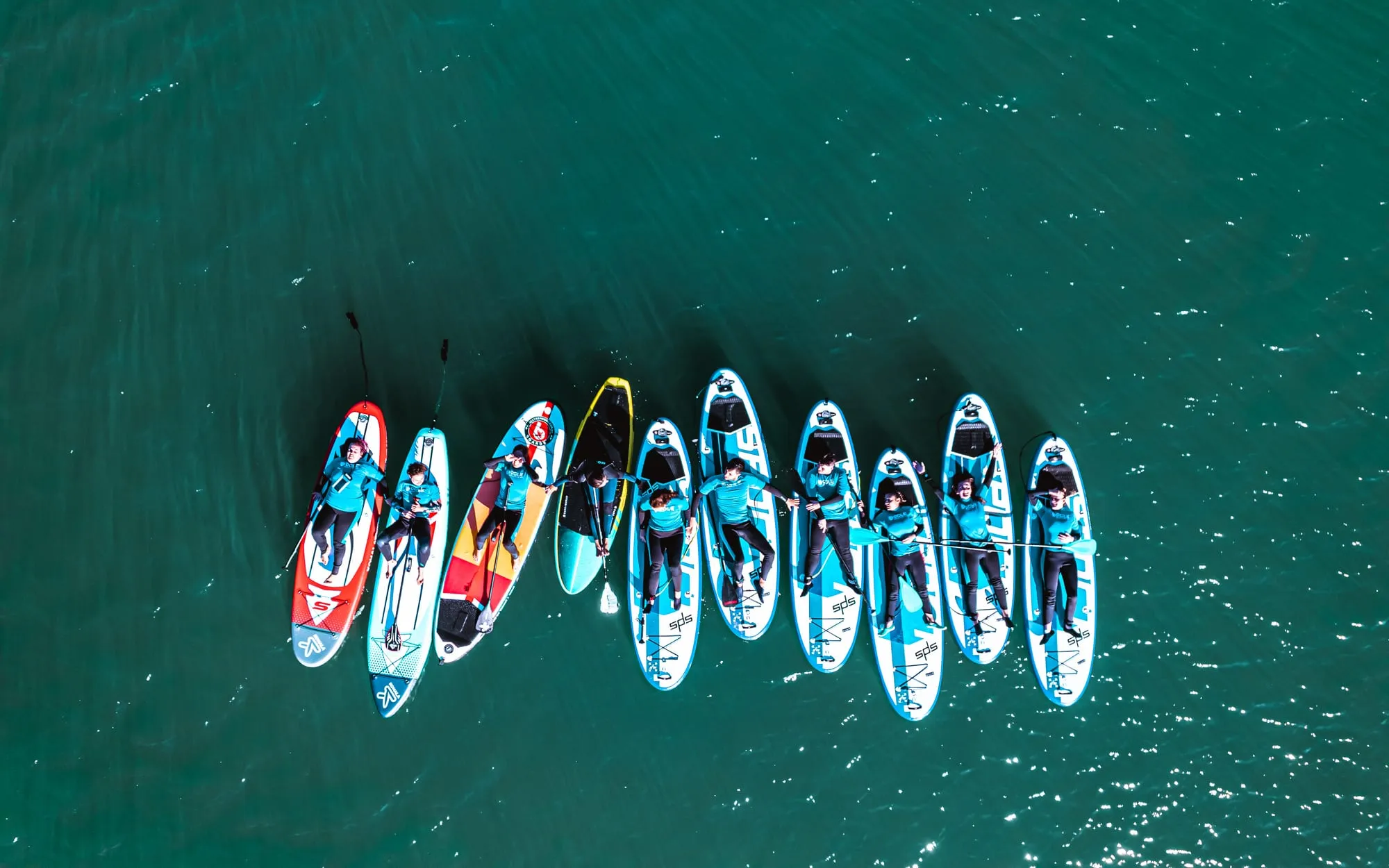 Vista aérea con dron de un grupo de once tablas de paddle surf en fila sobre el agua verde de la ría