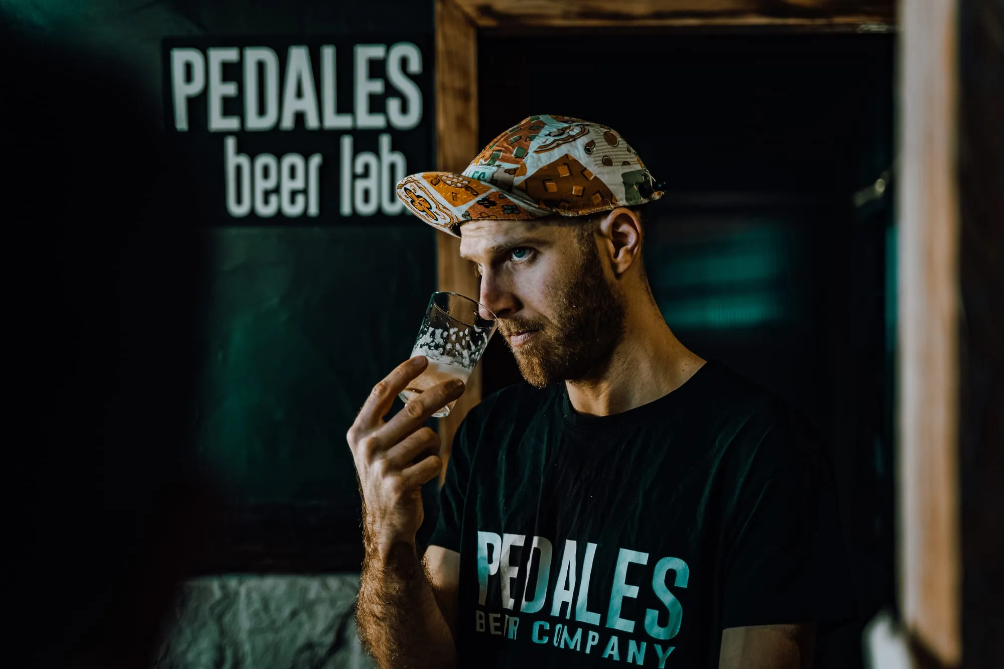 El cervecero de Pedales huele una cerveza recién tirada con el cartel Pedales beer lab detrás