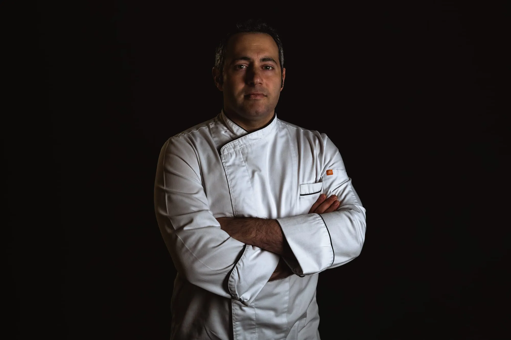 Retrato del chef Íñigo Veci con chaquetilla blanca y los brazos cruzados sobre fondo negro