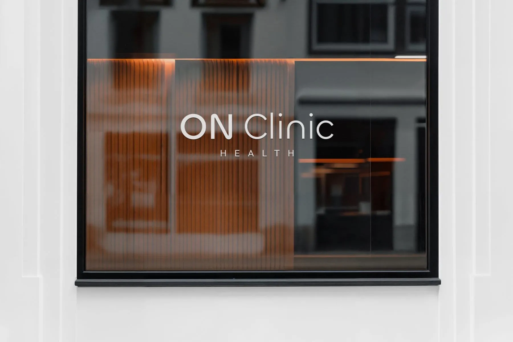 Rótulo ON Clinic Health sobre la cristalera del local, con el interior de madera cálida detrás