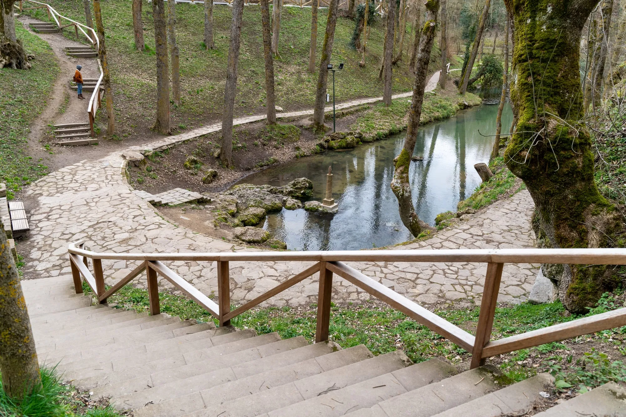 Nacimiento del Ebro en Fontibre visto desde la escalera, con la poza, la senda empedrada y una persona en el camino