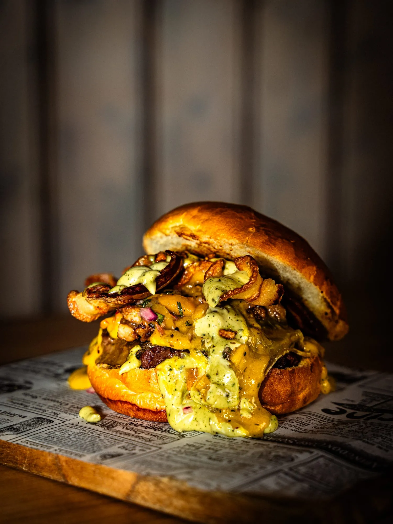 Hamburguesa con bacon y salsa de queso desbordando sobre tabla de madera, fondo oscuro