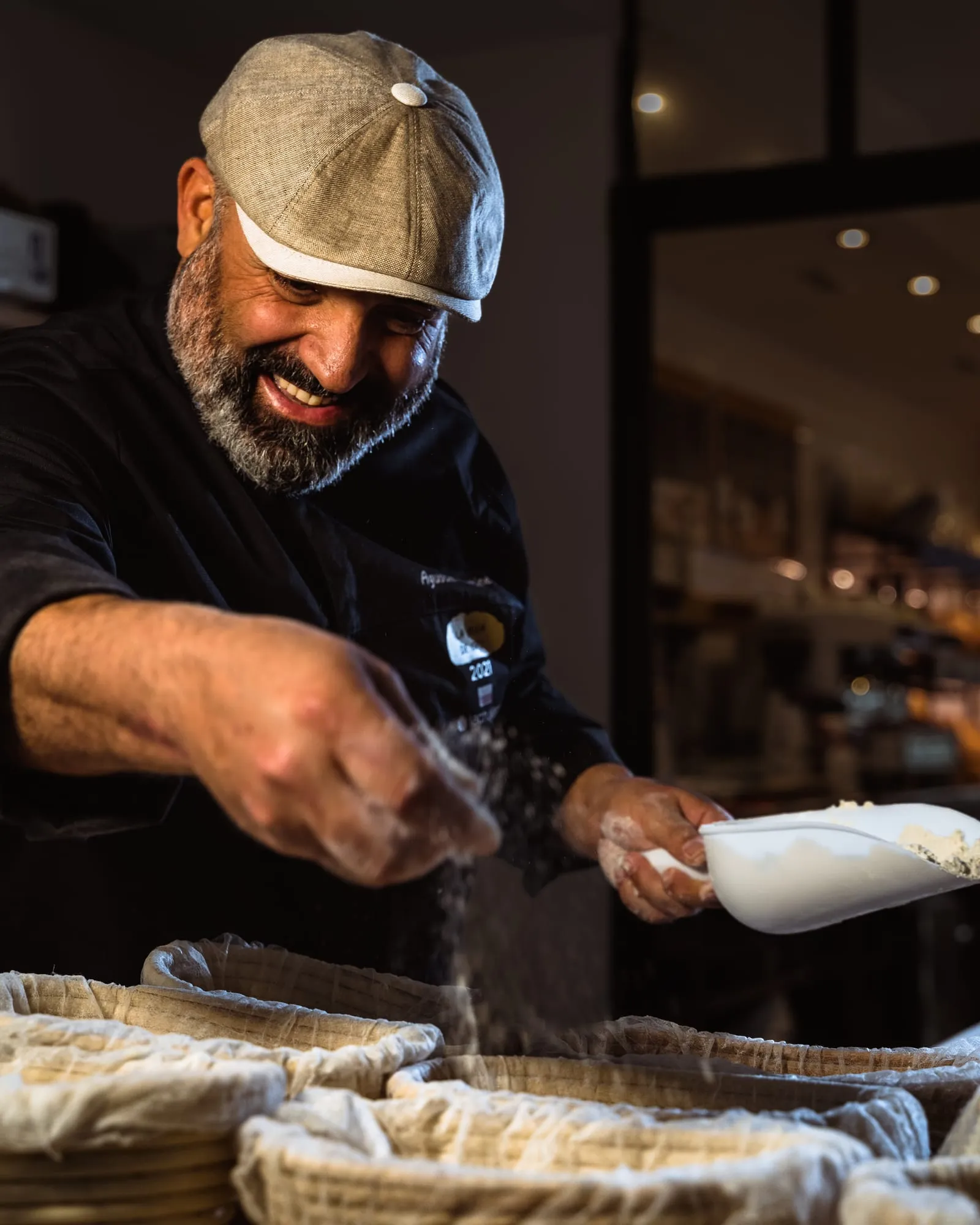 El panadero sonríe mientras lanza un puñado de harina sobre los banetones con masa