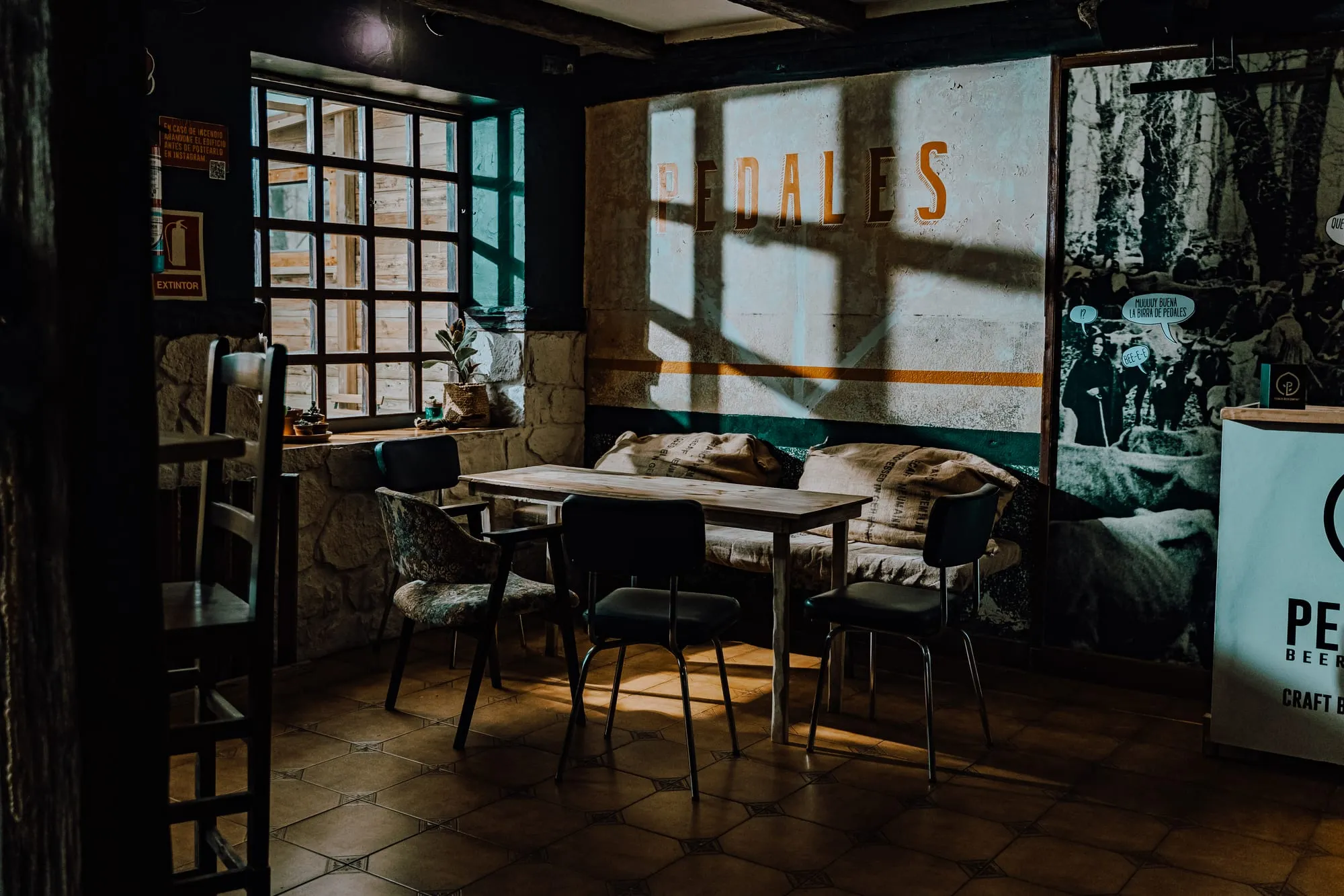 Sala del taproom con la palabra Pedales pintada en la pared, mesa de madera y mural fotográfico antiguo