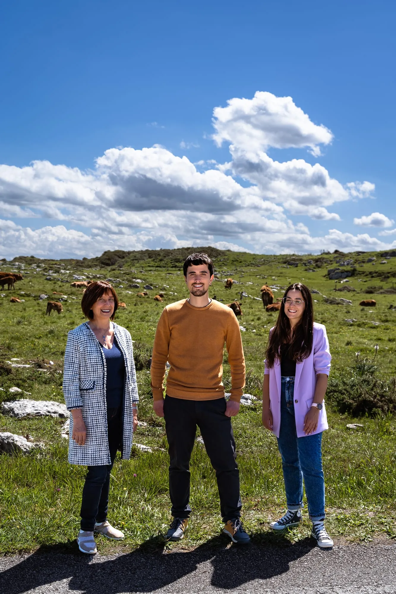 Tres integrantes de la candidatura en un prado con vacas bajo un cielo azul con nubes