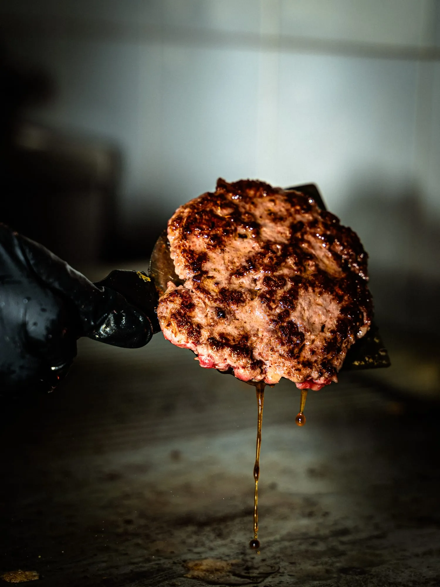 Mano con guante negro sosteniendo una hamburguesa de carne cruda sobre fondo negro