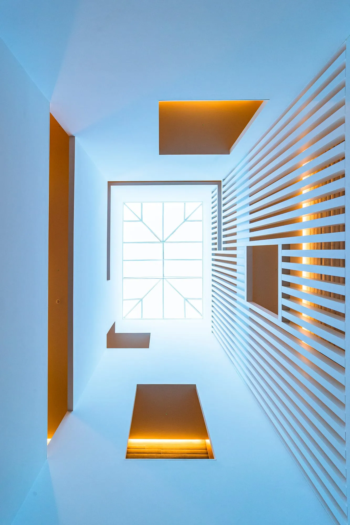 Pozo de luz entre lamas de madera y hormigón, mirando hacia el cielo desde la escalera