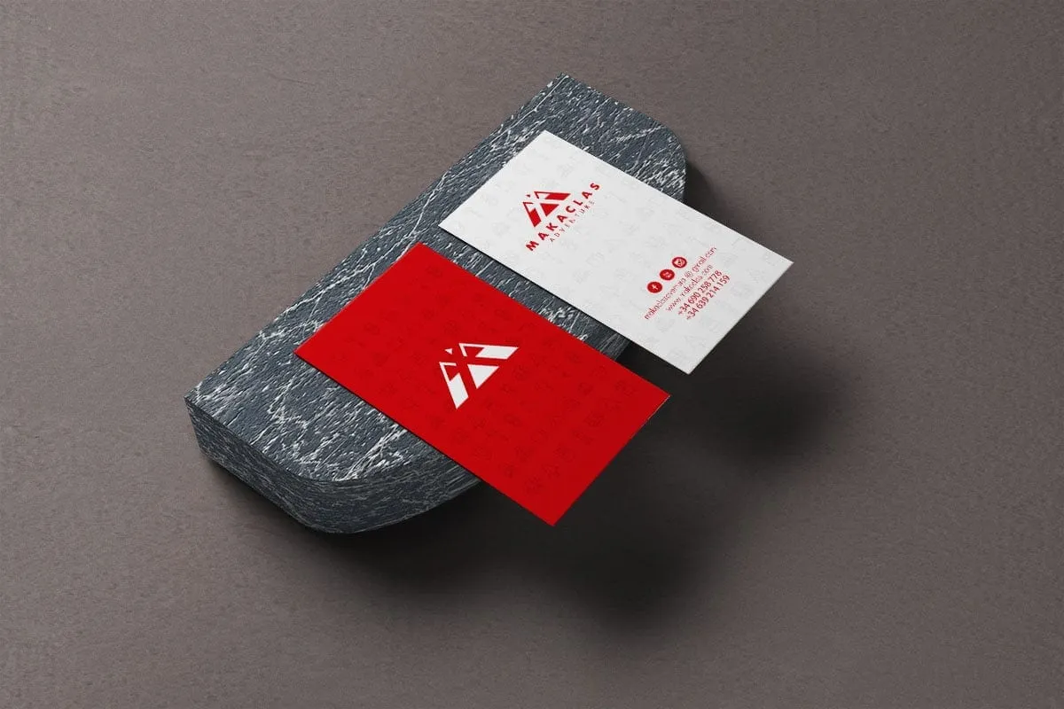 Tarjetas de visita de Makaclas, una roja y otra blanca con iconos de montaña, sobre una piedra oscura