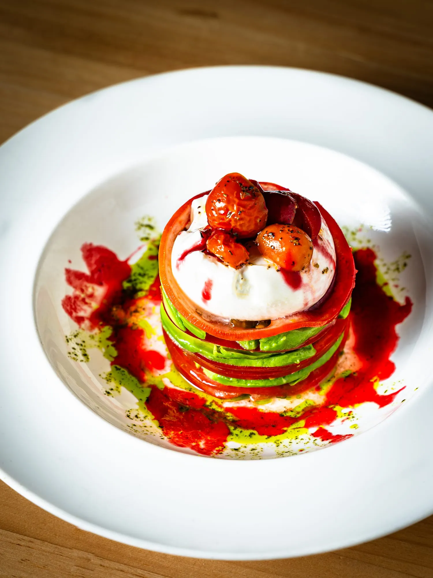 Torre de tomate, aguacate y burrata con tomates cherry, coulis rojo y aceite de hierbas
