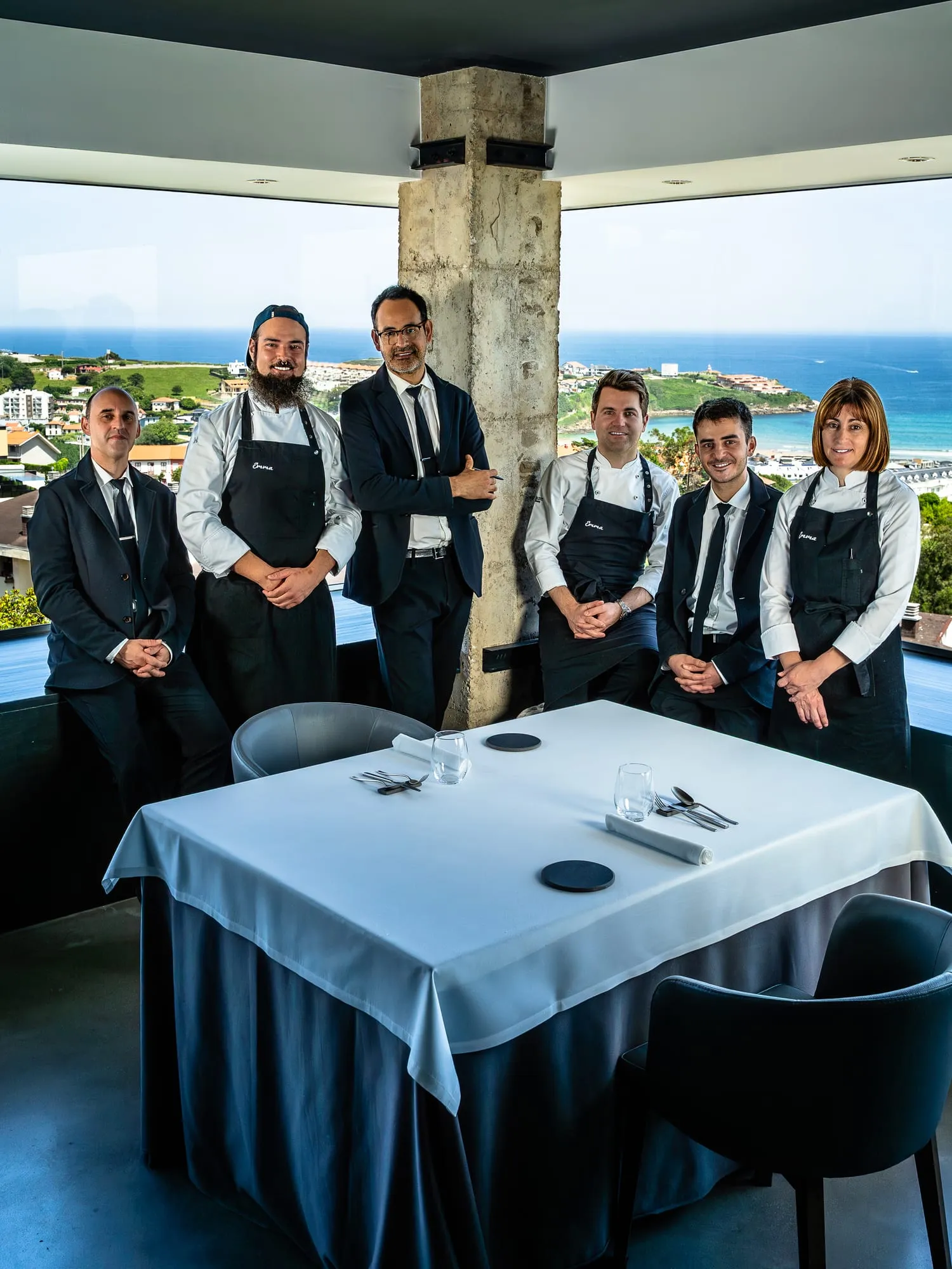 El equipo de sala y cocina de Emma posa junto a una mesa con el mar de Suances detrás