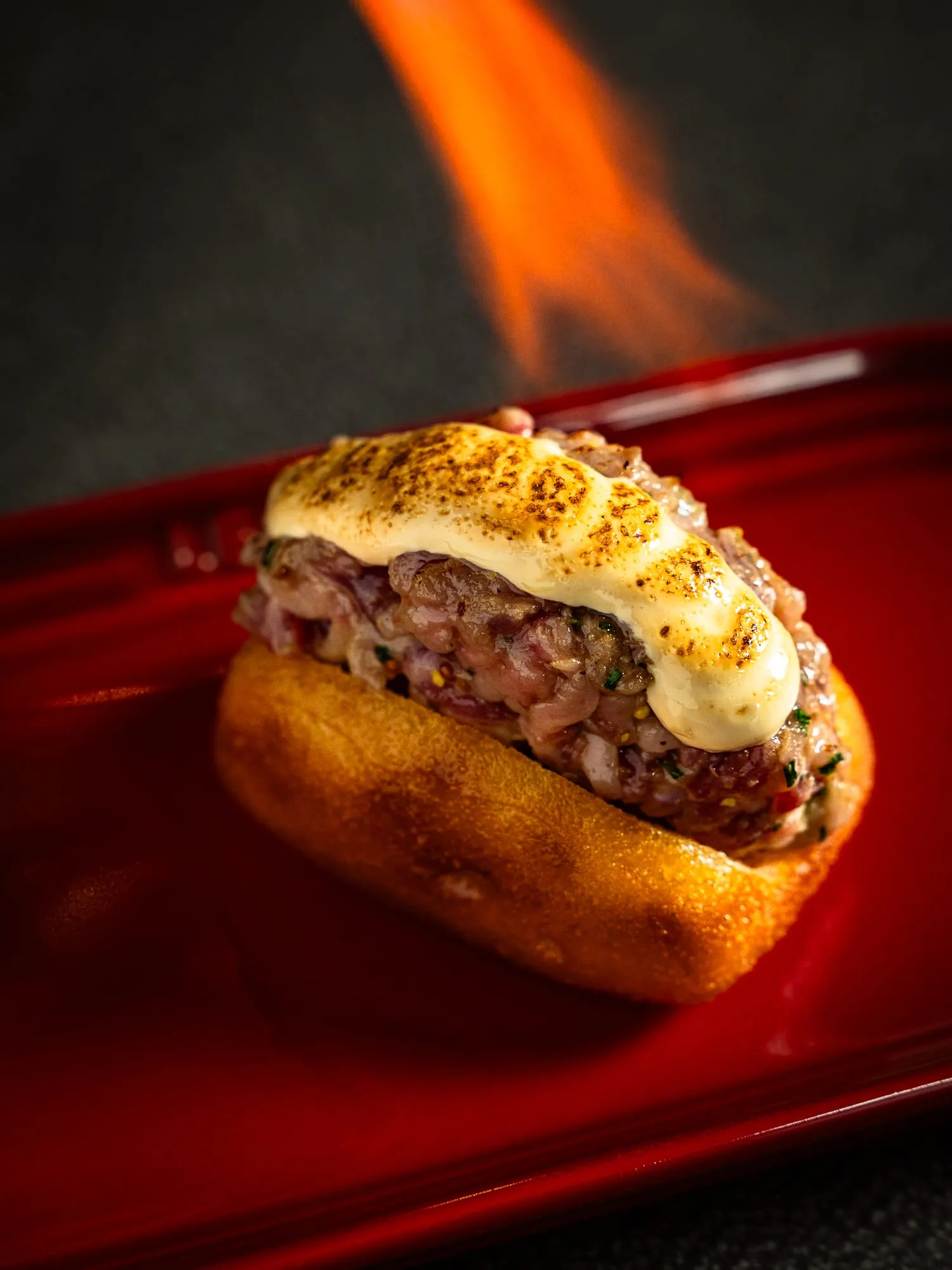 Bollo relleno gratinado flambeándose con llama sobre un plato rojo
