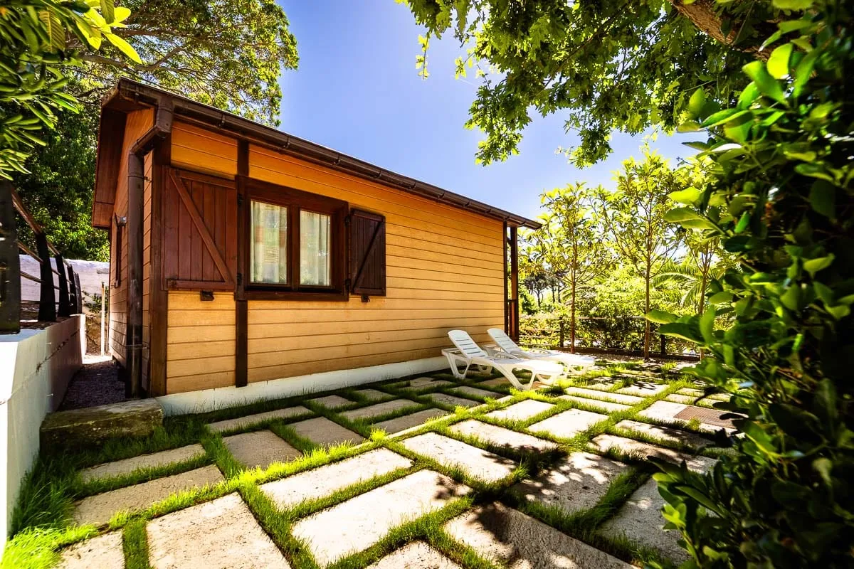 Bungalow de madera para cuatro personas con tumbonas en el césped a la sombra de los árboles