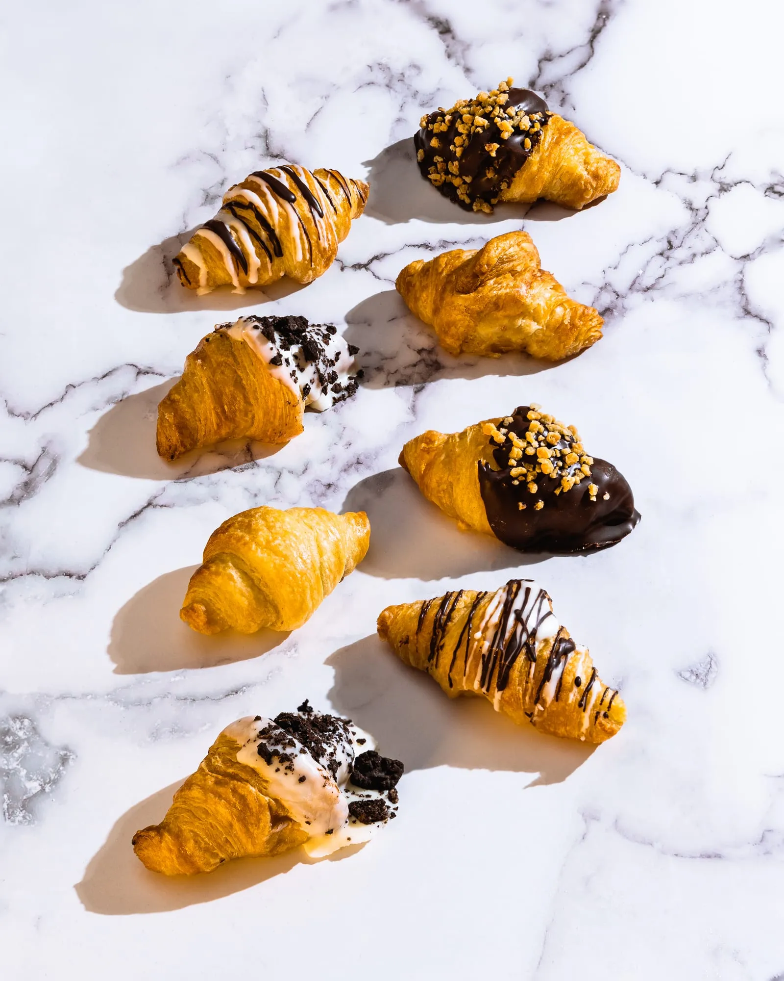 Ocho minicroissants sobre mármol blanco con chocolate, galleta y crocanti de frutos secos