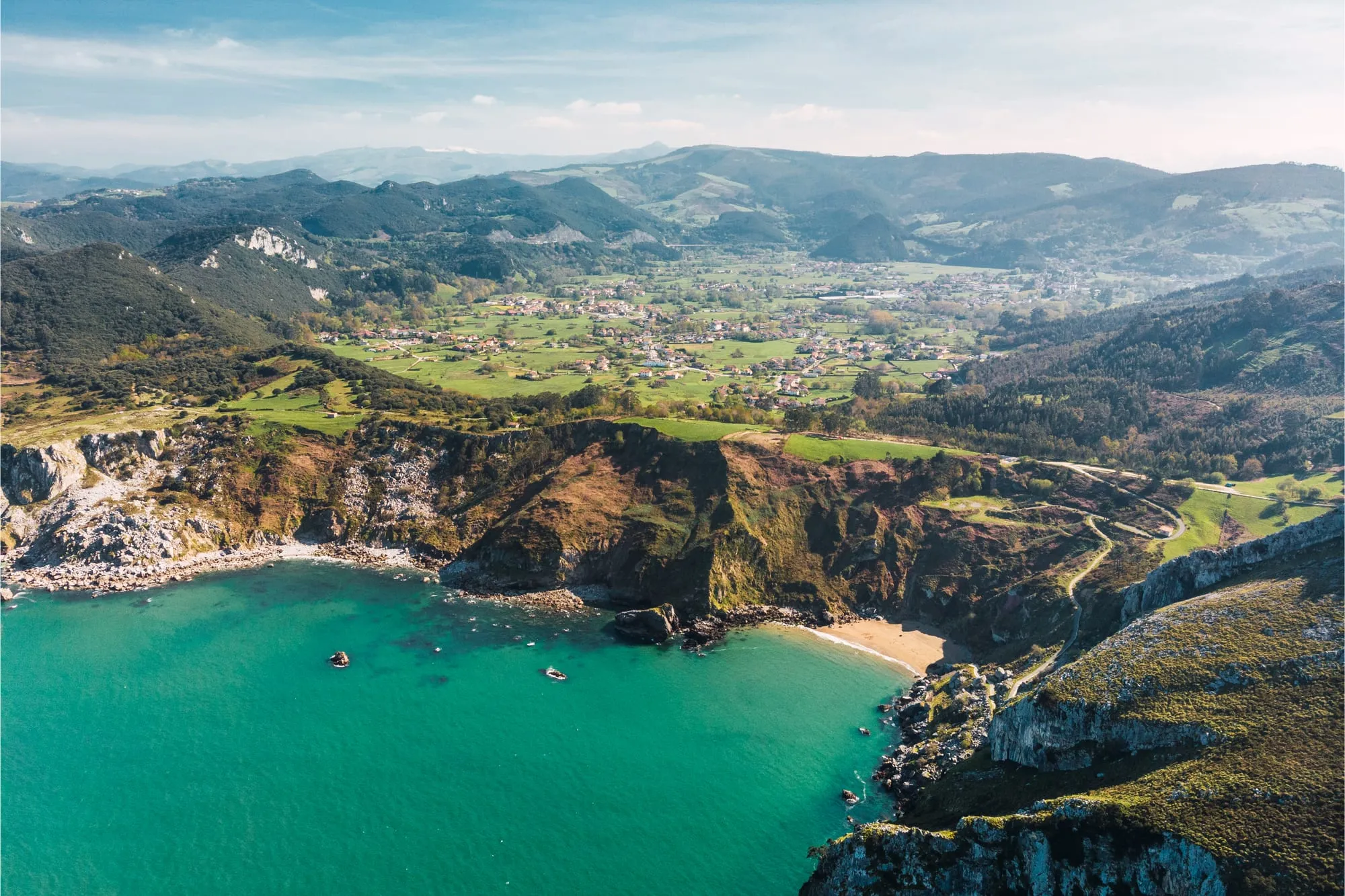 Cala de agua turquesa entre acantilados y el valle de Liendo con sus pueblos, a vista de dron
