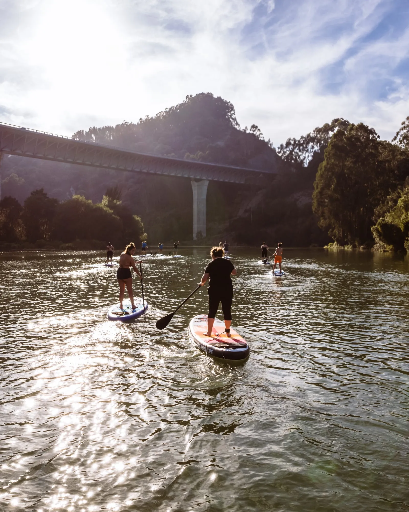 Dos personas reman a contraluz por el río hacia el viaducto, con el sol reflejado en el agua