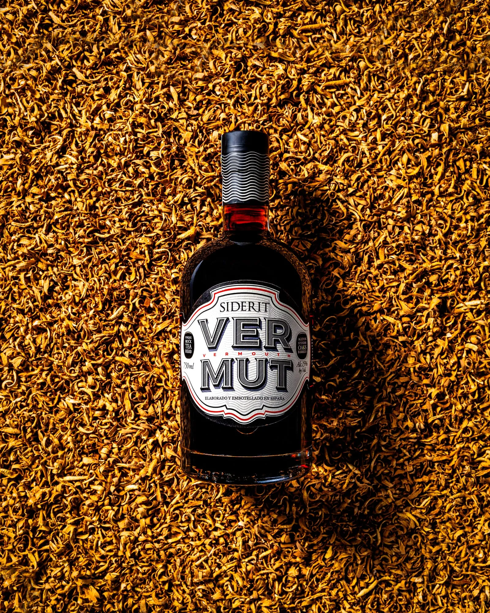 Botella de vermut Siderit sobre un lecho de virutas de roble iluminado con luz cálida