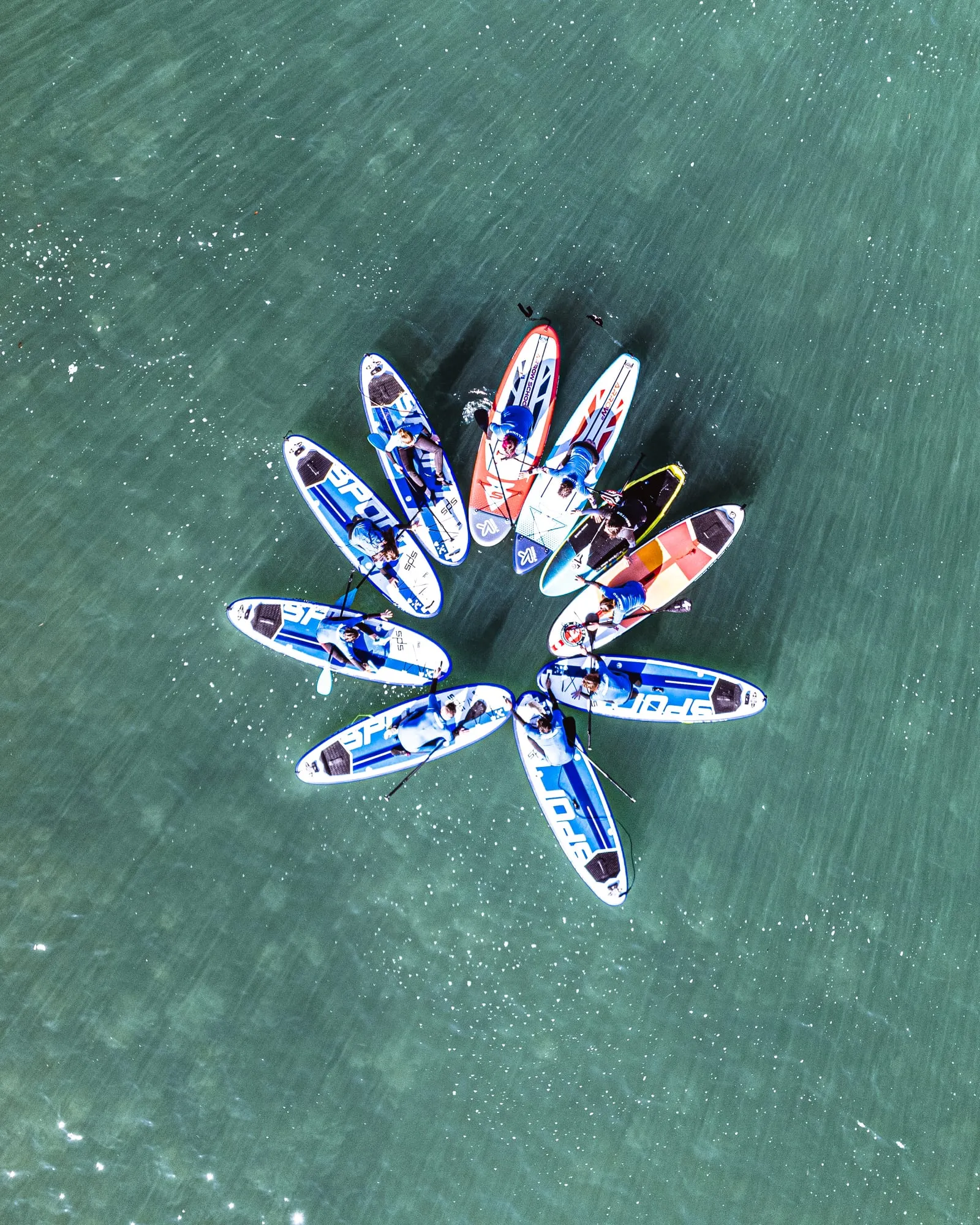 Grupo de tablas de paddle surf formando una estrella sobre el agua verde, visto desde el dron