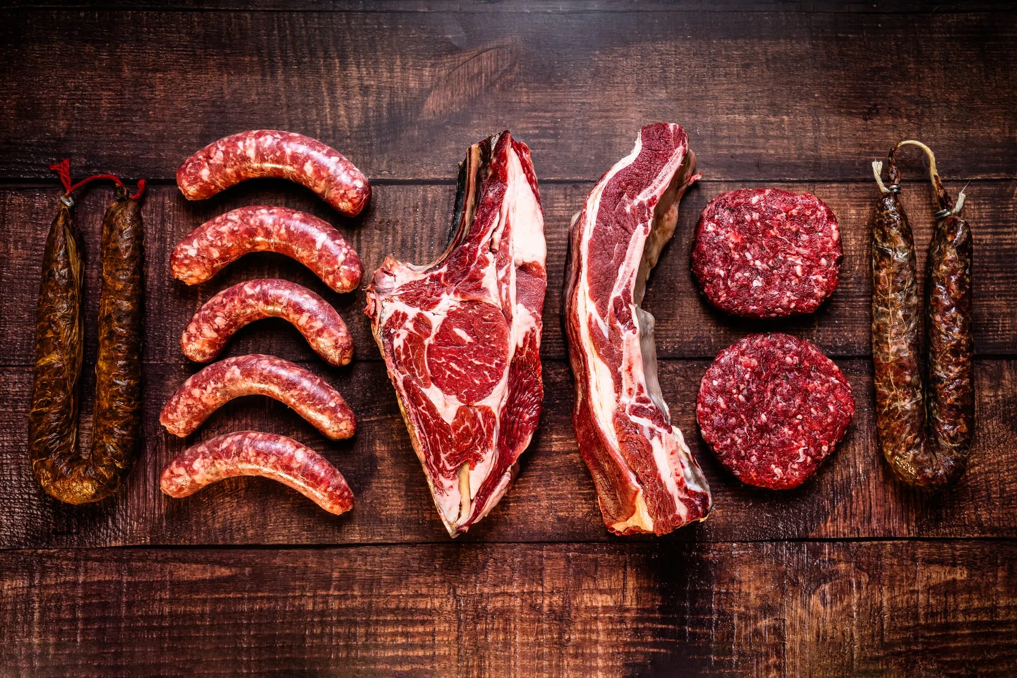 Chorizos, salchichas, chuletón, costilla y hamburguesas de tudanca alineados sobre una tabla de madera oscura