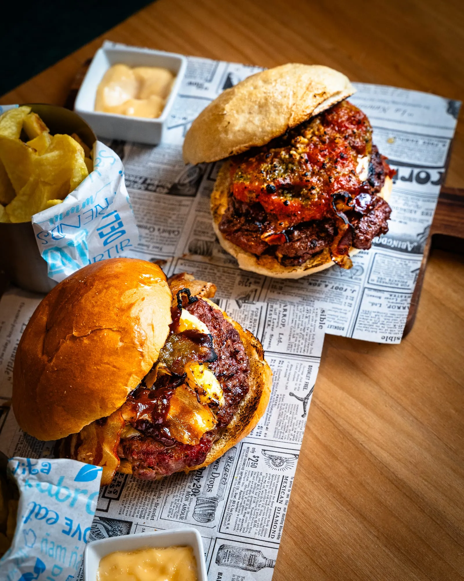Hamburguesa sobre papel de periódico con bolsa de patatas fritas y salsa