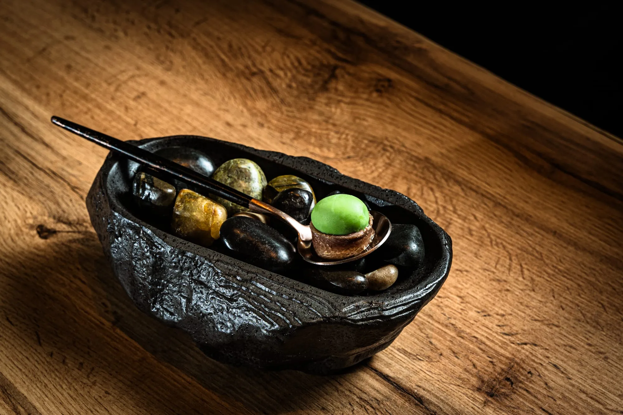 Aperitivo servido en un cuenco de piedra negra con cuchara de cobre sobre una mesa de madera