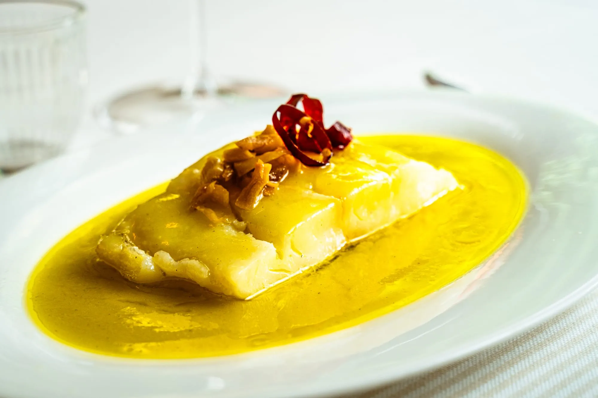 Lomo de pescado blanco sobre salsa amarilla de aceite con ajos dorados y guindilla