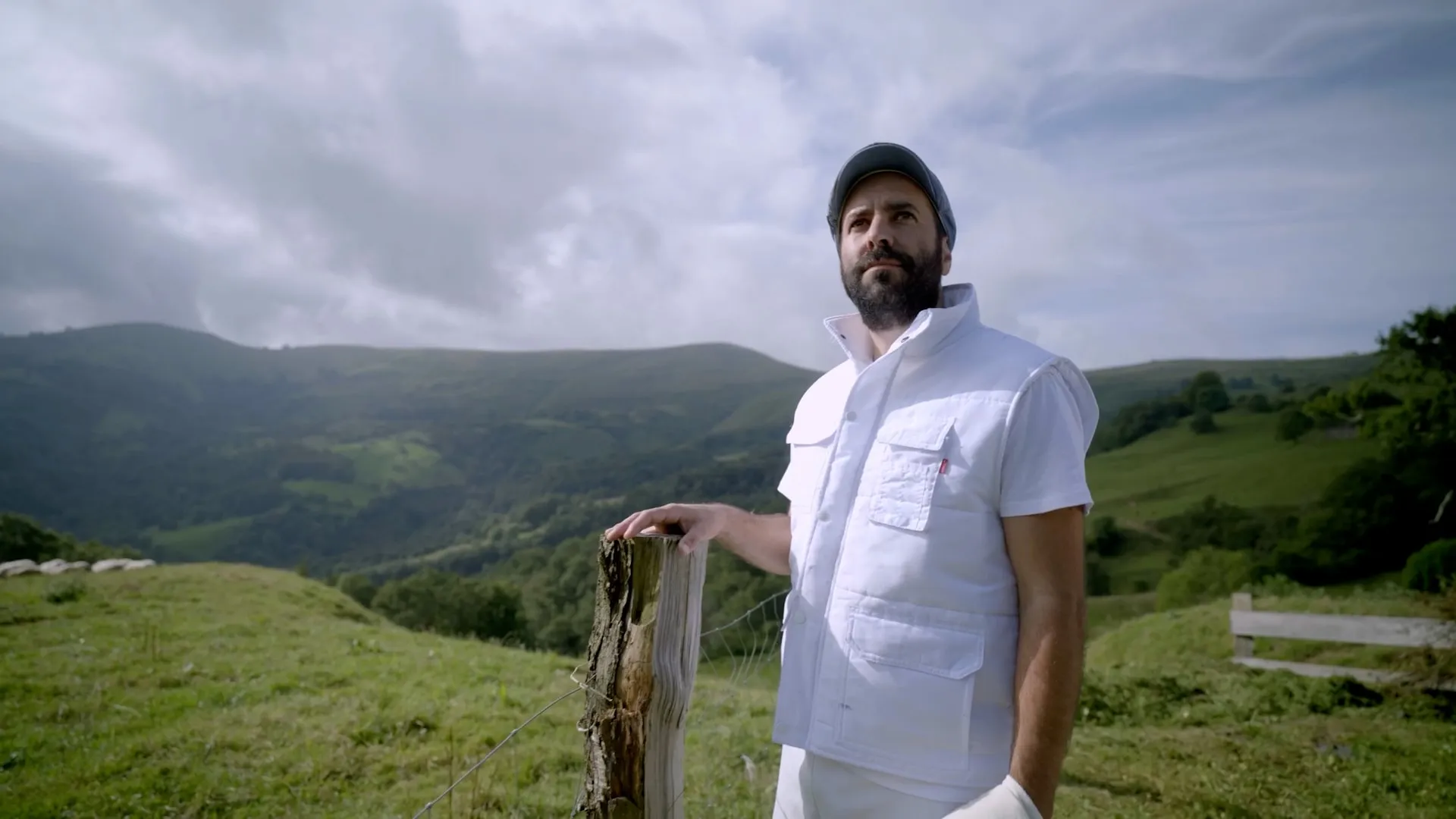 Un productor posa en un prado de montaña con el valle de fondo