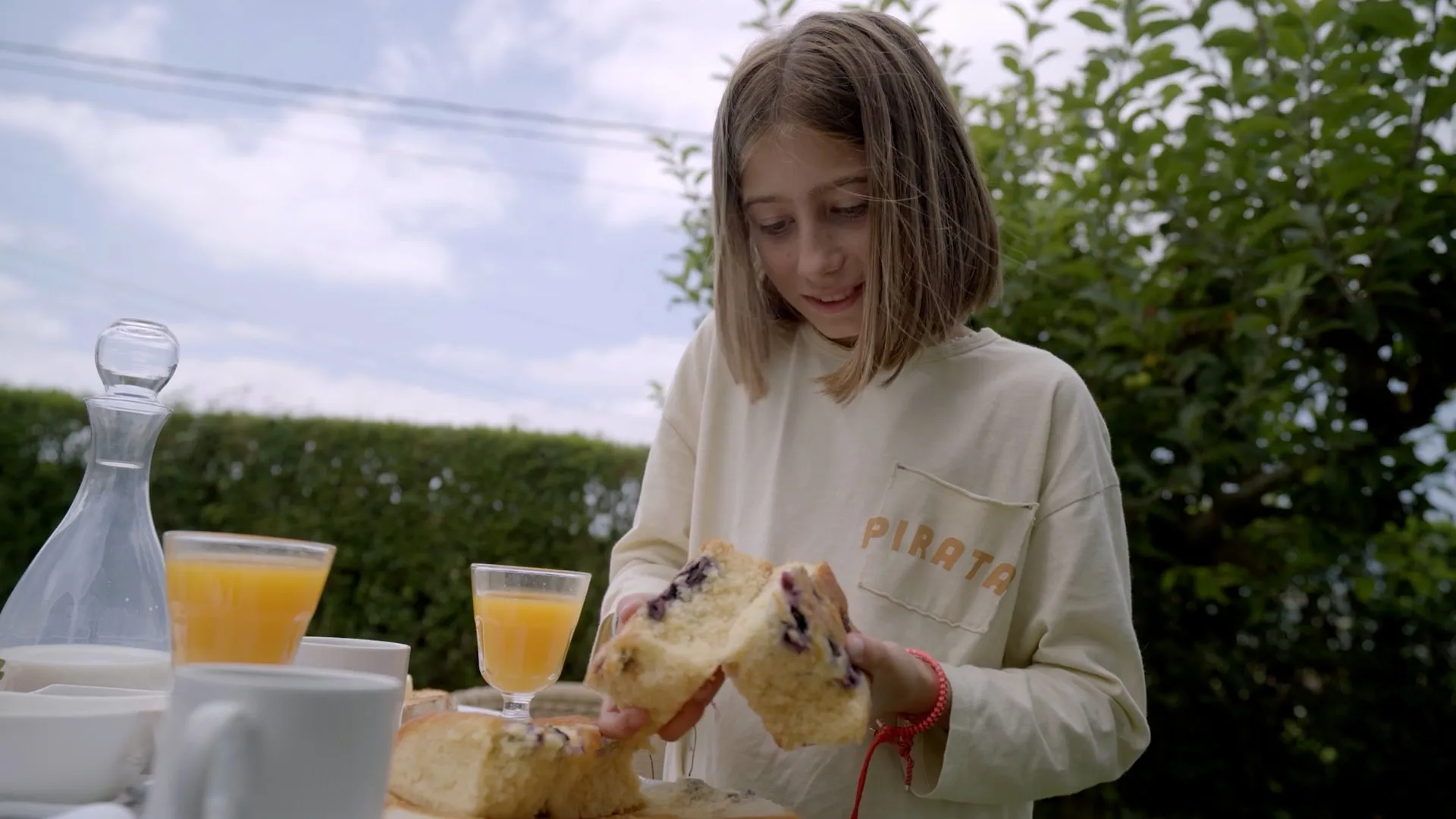 Una niña parte un bizcocho de arándanos en la mesa del desayuno en el jardín