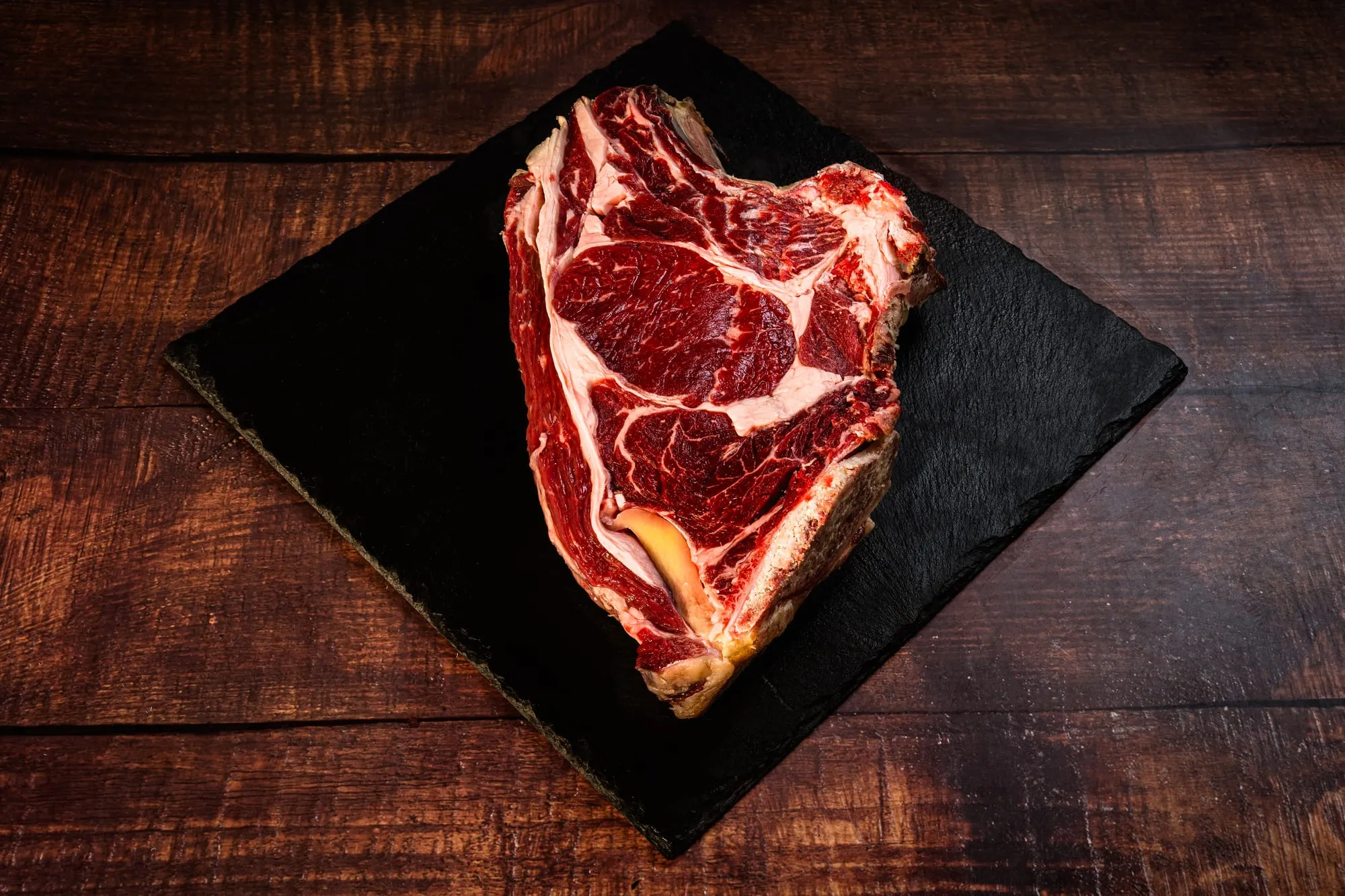 Chuletón de tudanca crudo con su veteado sobre pizarra negra y madera