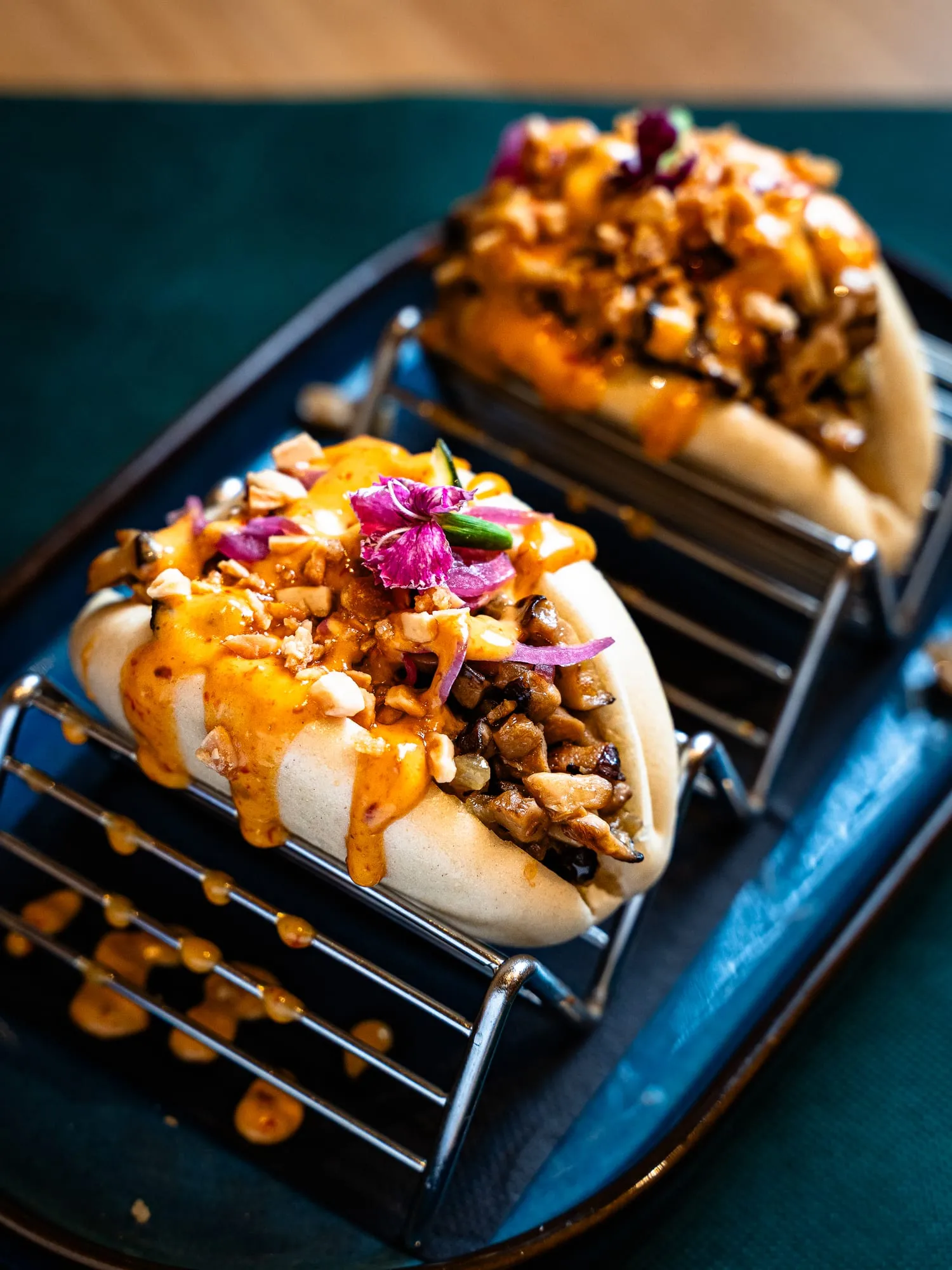Dos panes bao rellenos con salsa picante, cacahuete, cebolla encurtida y flor comestible