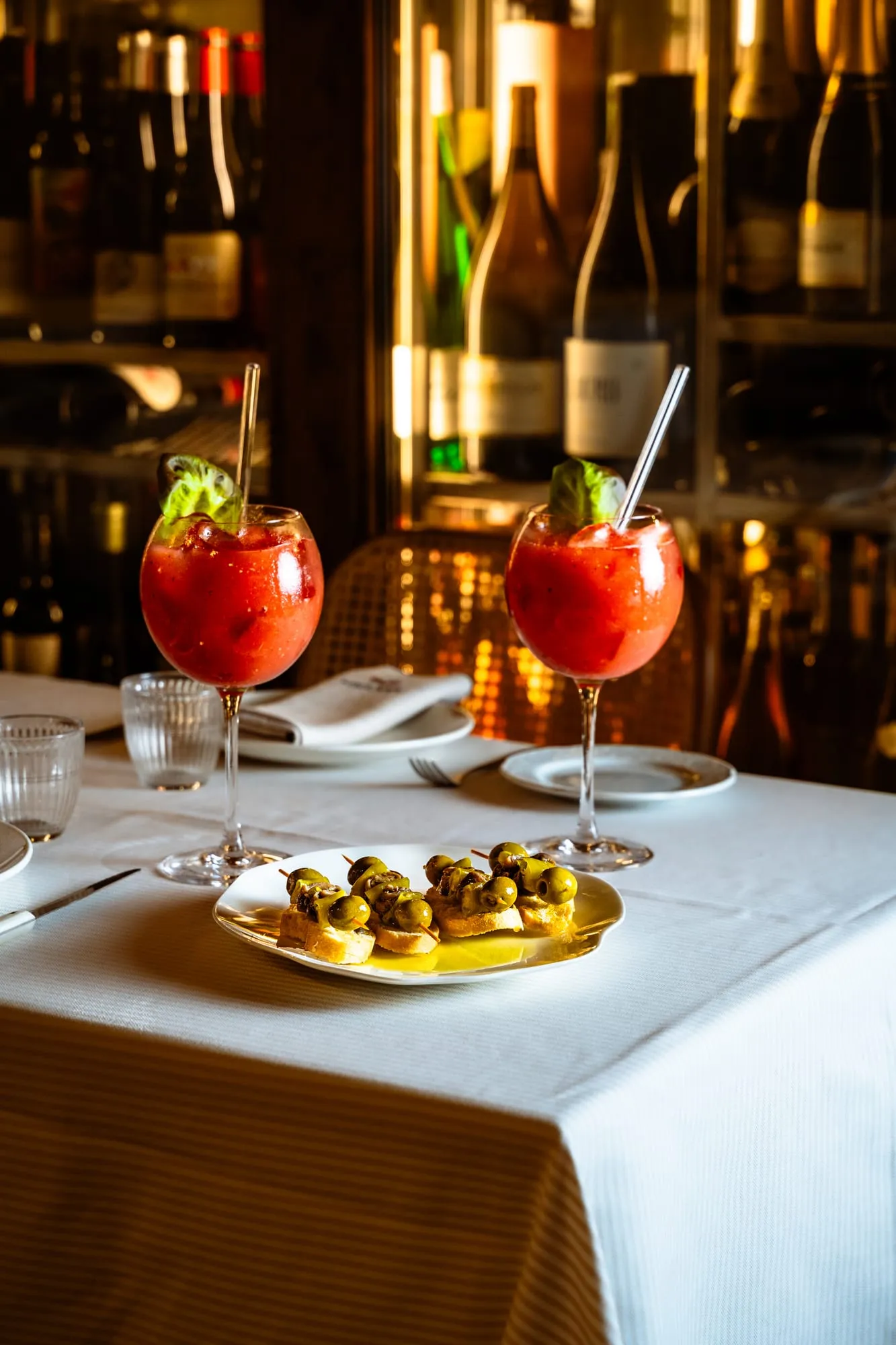 Dos bloody mary con albahaca y un plato de pinchos de aceitunas ante la vinoteca iluminada