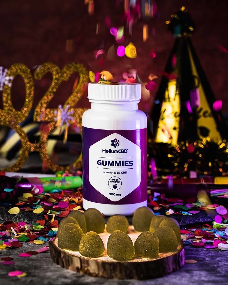 Bote de gominolas HeliumCBD rodeado de gominolas sobre una rodaja de madera, con confeti, gorro de fiesta y el número 2022 dorado