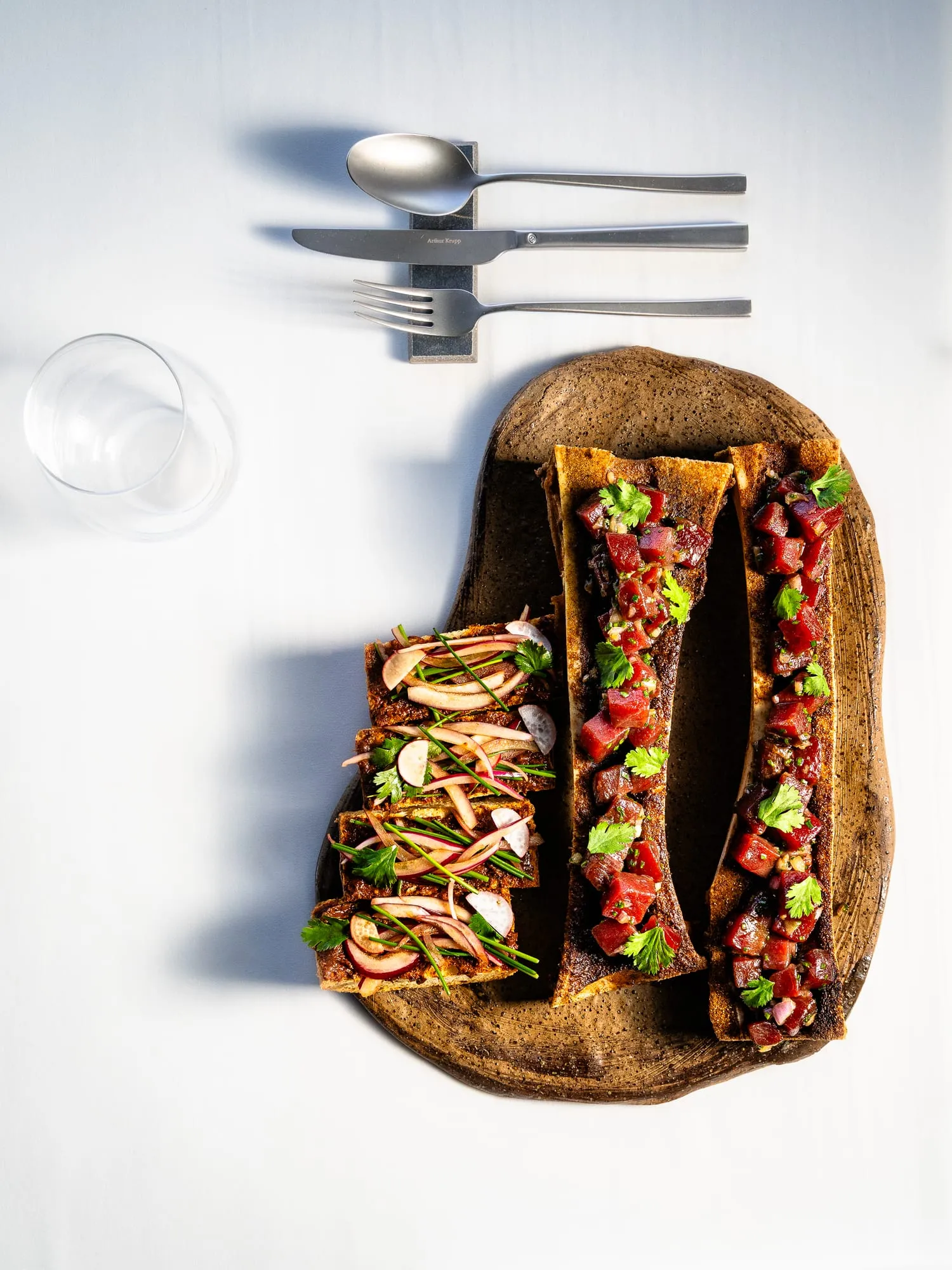 Tostadas alargadas con tartar de atún y verduras crujientes sobre una tabla de madera, vistas desde arriba