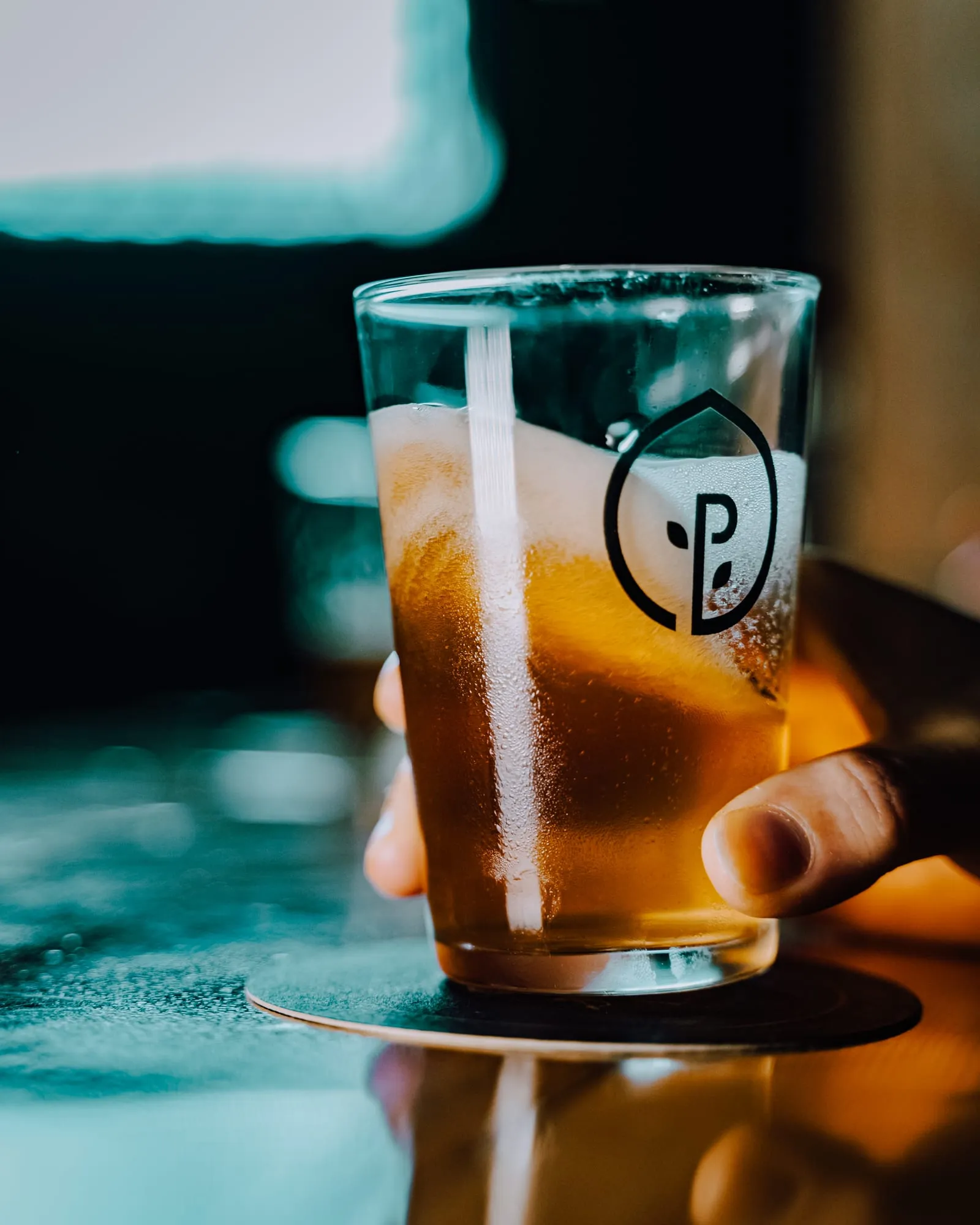 Vaso de pinta con el logotipo de Pedales lleno de cerveza ámbar a contraluz