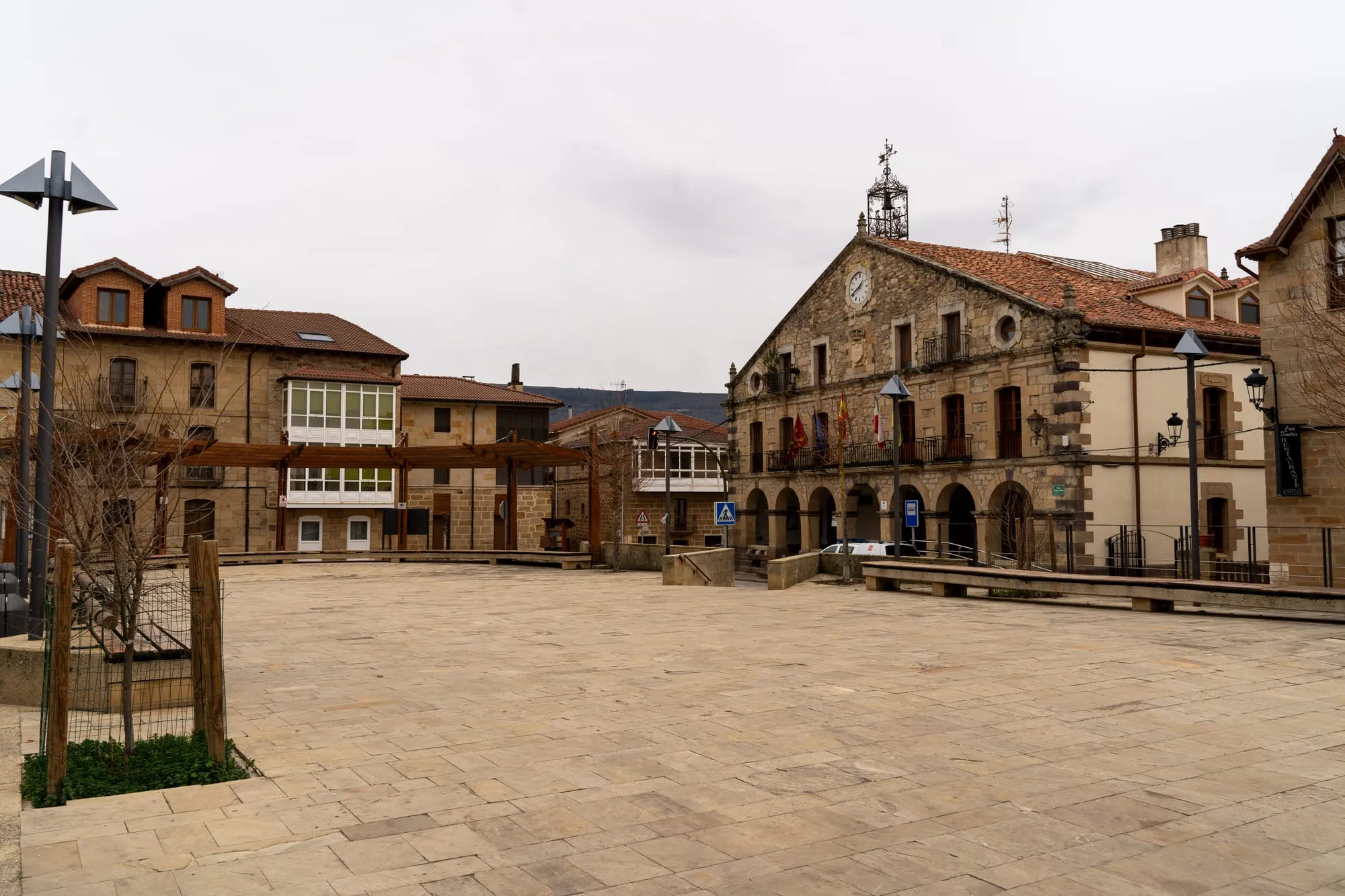 Plaza mayor de Polientes vacía, con el ayuntamiento de piedra, el reloj y las banderas en el balcón
