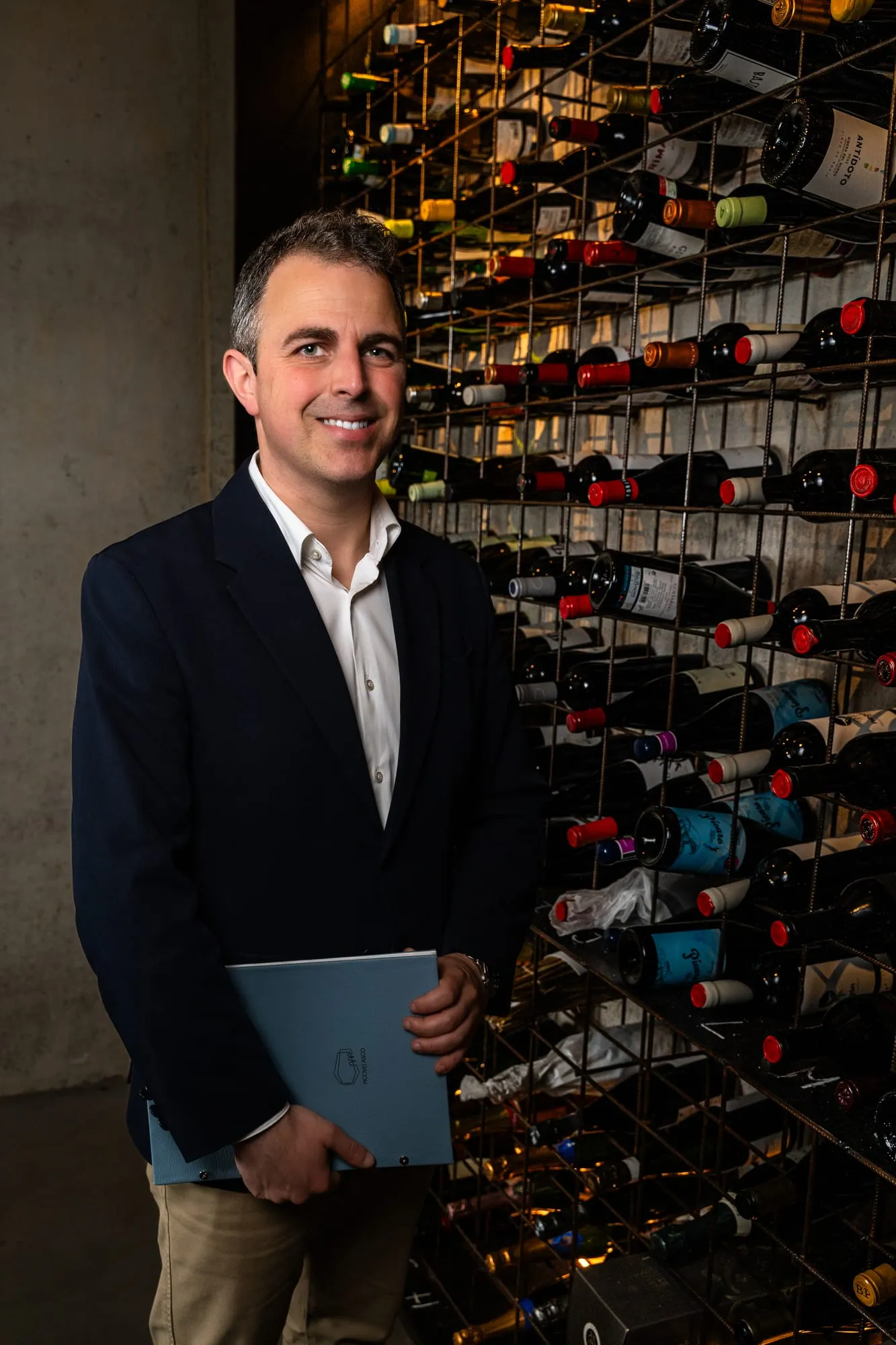 Sumiller con una carta en la mano frente a la pared de botellas de la bodega