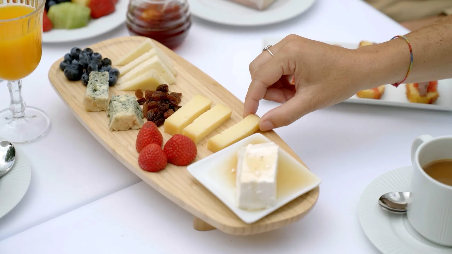 Una mano coge un trozo de queso de una tabla con fresas, arándanos y quesos de Cantabria
