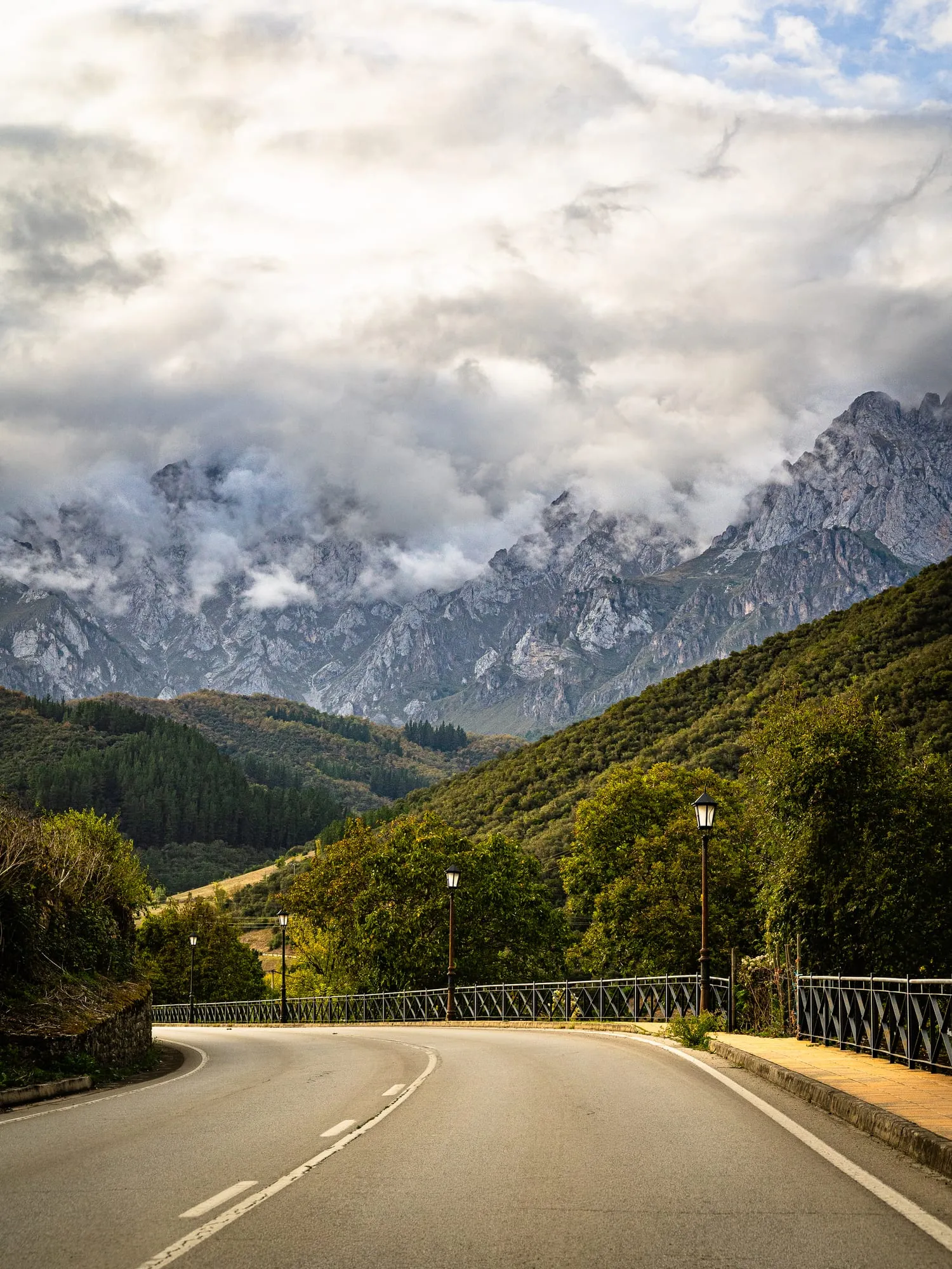 Carretera que entra en el valle, con los Picos de Europa entre nubes al fondo