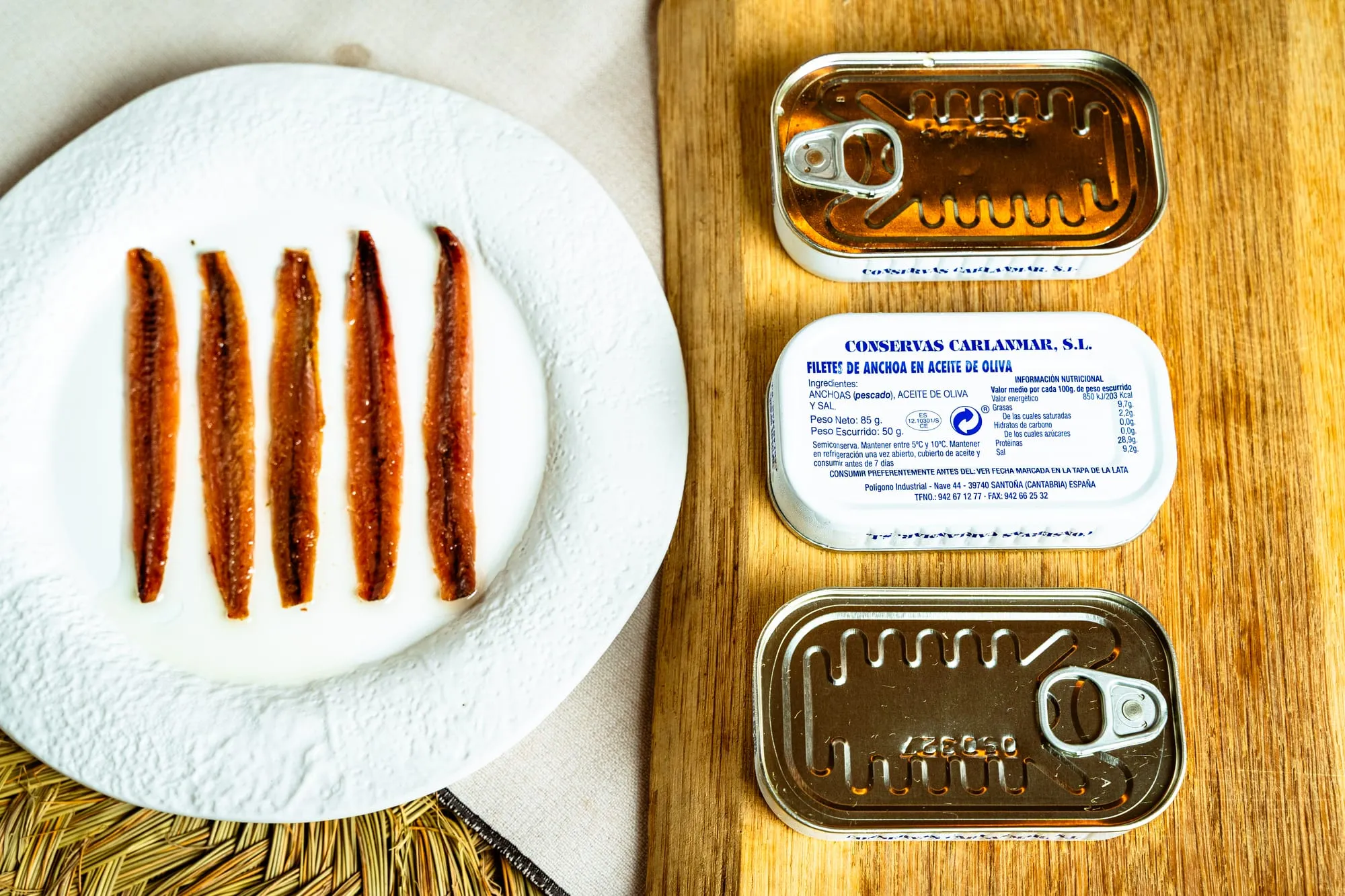 Cinco filetes de anchoa de Santoña en plato blanco junto a dos latas de conservas