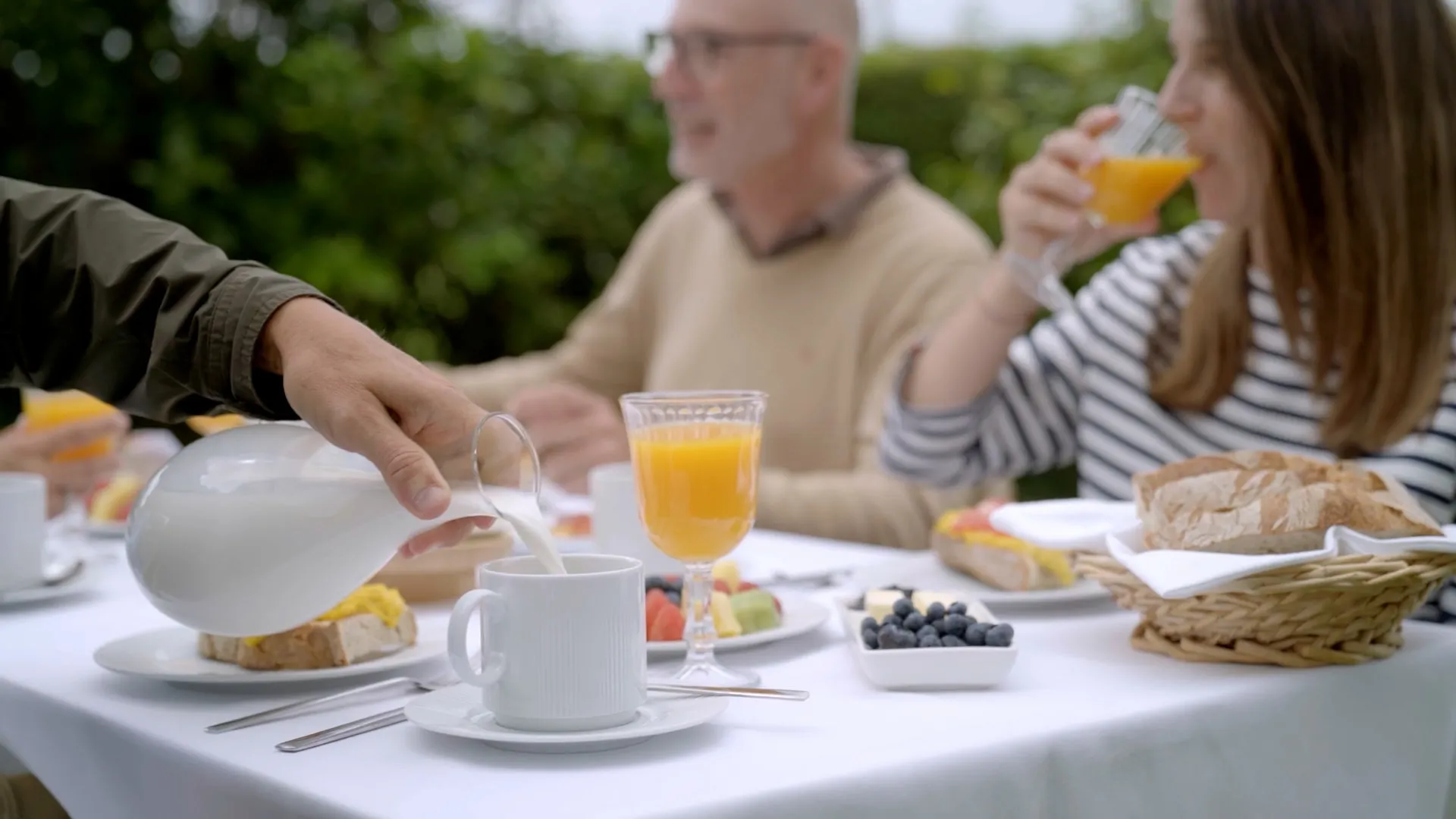 Desayuno en el jardín: sirven leche mientras una chica bebe zumo de naranja