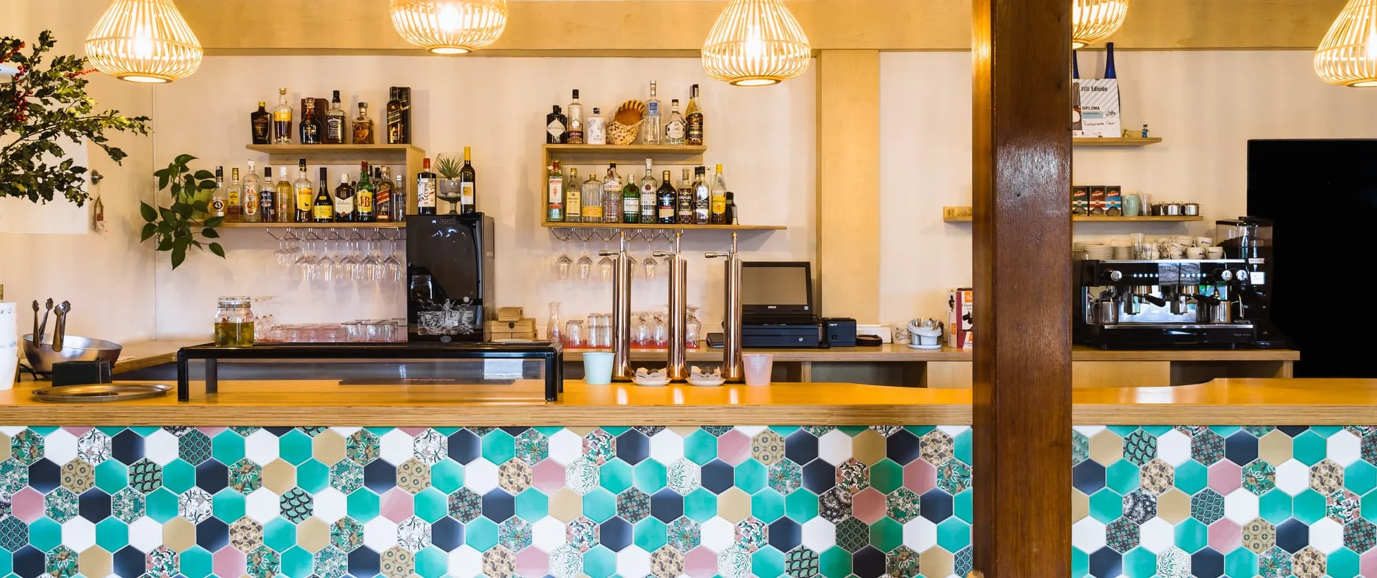 Barra del restaurante con azulejos hexagonales de colores, lámparas de mimbre y botellas