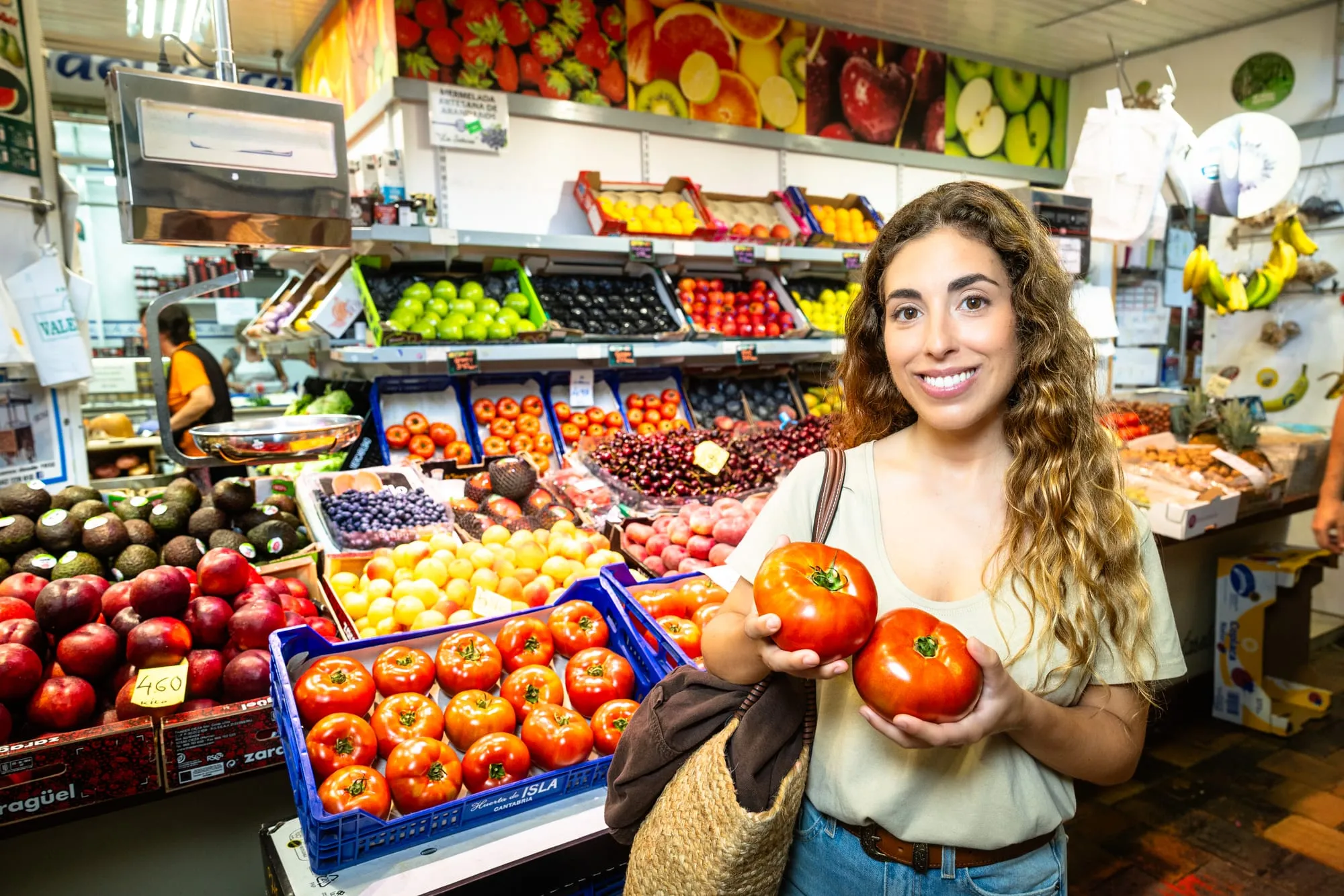 La protagonista sonríe con dos tomates en la mano en un puesto de fruta del mercado