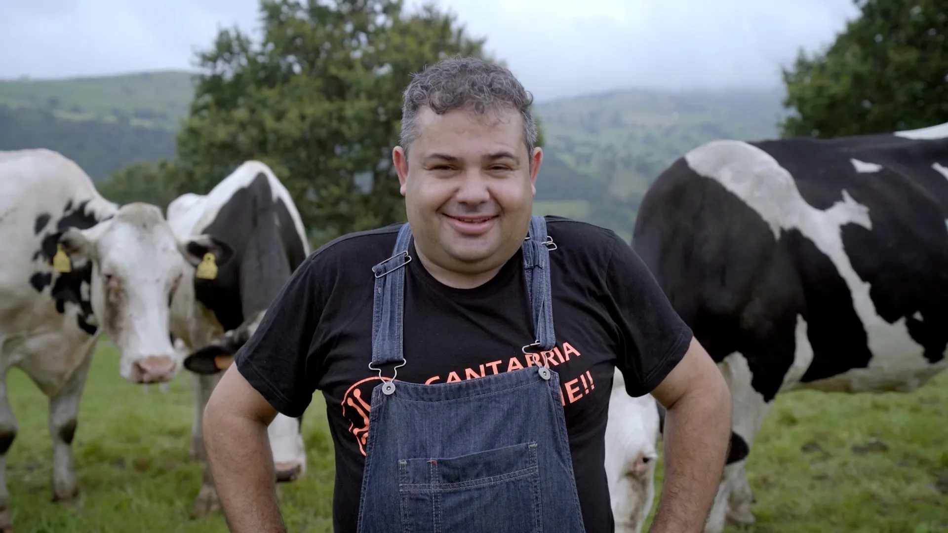 Un ganadero sonríe a cámara con sus vacas frisonas en el prado
