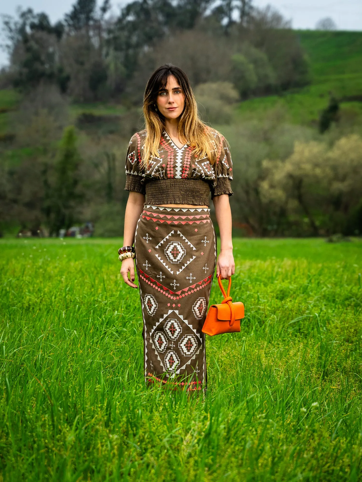 Modelo con blusa marrón estampada y falda larga de estampado étnico en un prado verde