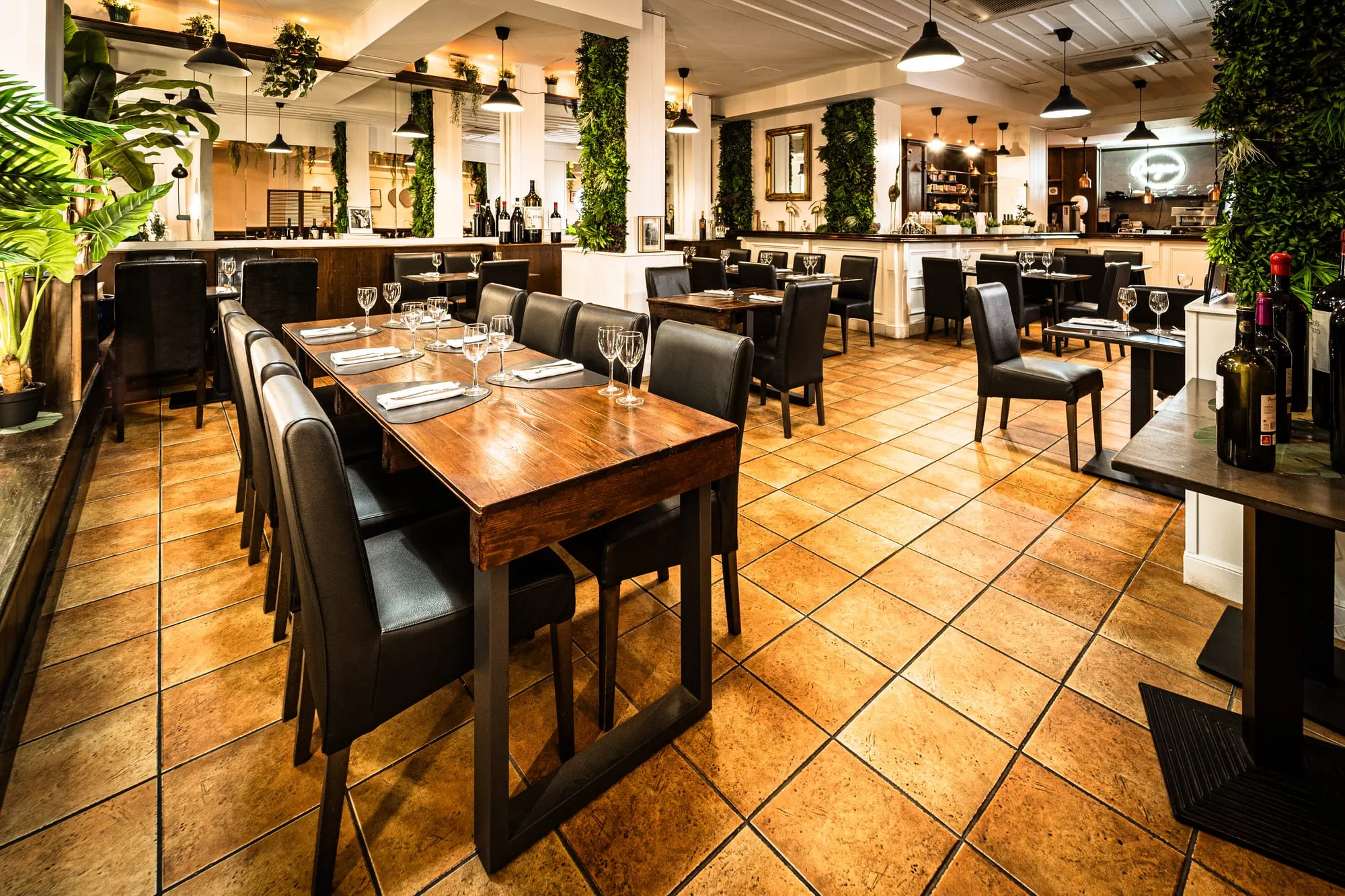 Comedor con mesas de madera, sillas de cuero negro y jardines verticales en las paredes